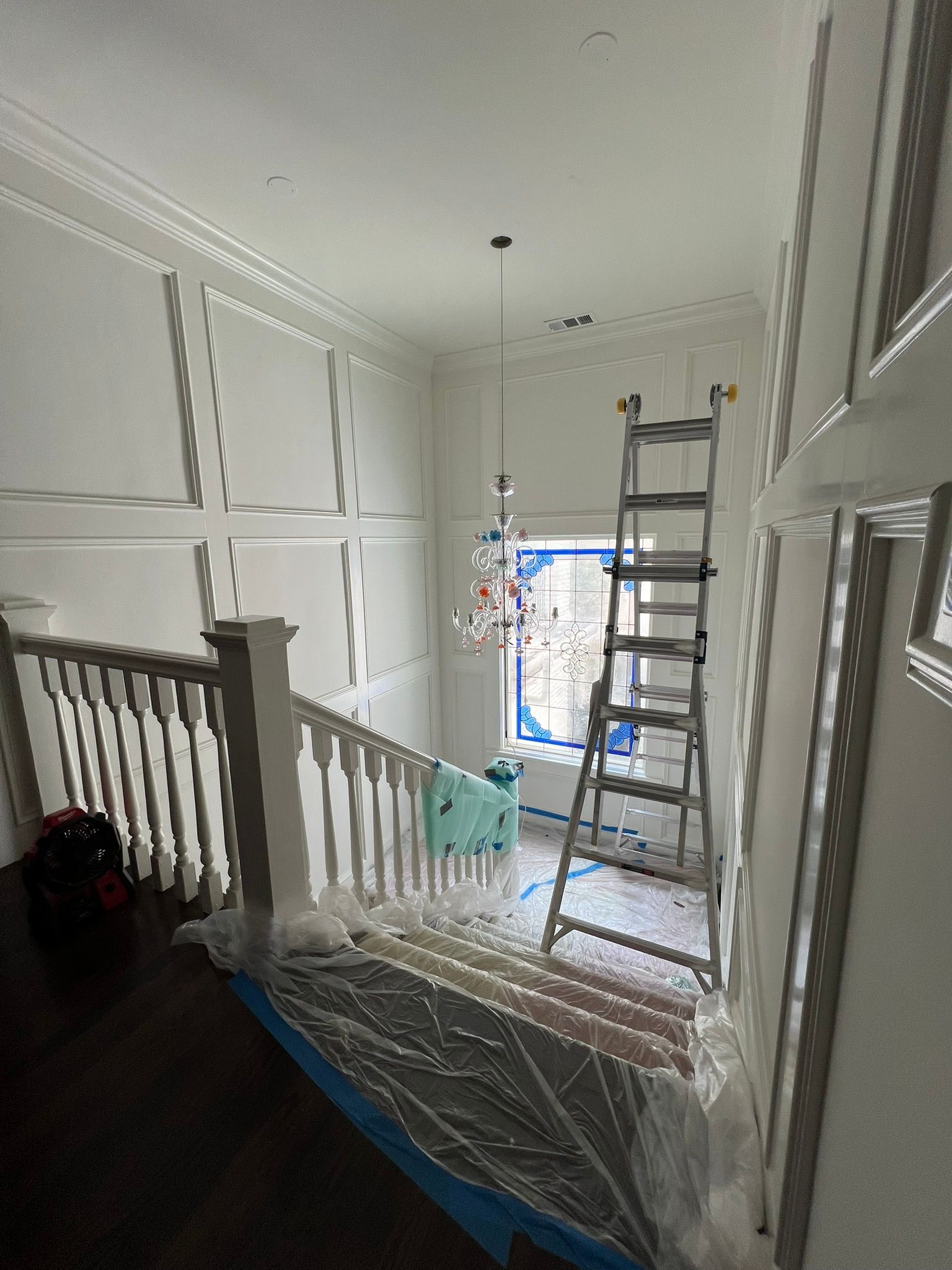 Interior hallway under renovation with ladders, plastic floor covering, and a window at the end.