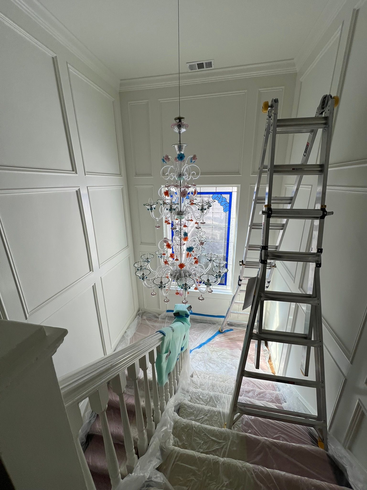 Stairwell with a metal ladder, white walls, and a decorated tree near a window at the landing