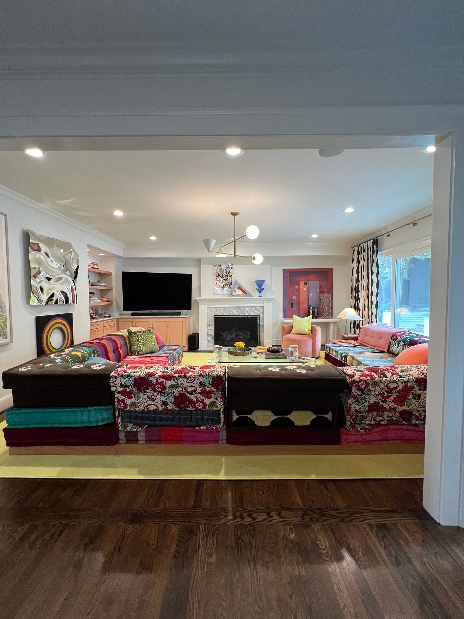Open living room with colorful sectional sofa, fireplace, large TV, and recessed lighting