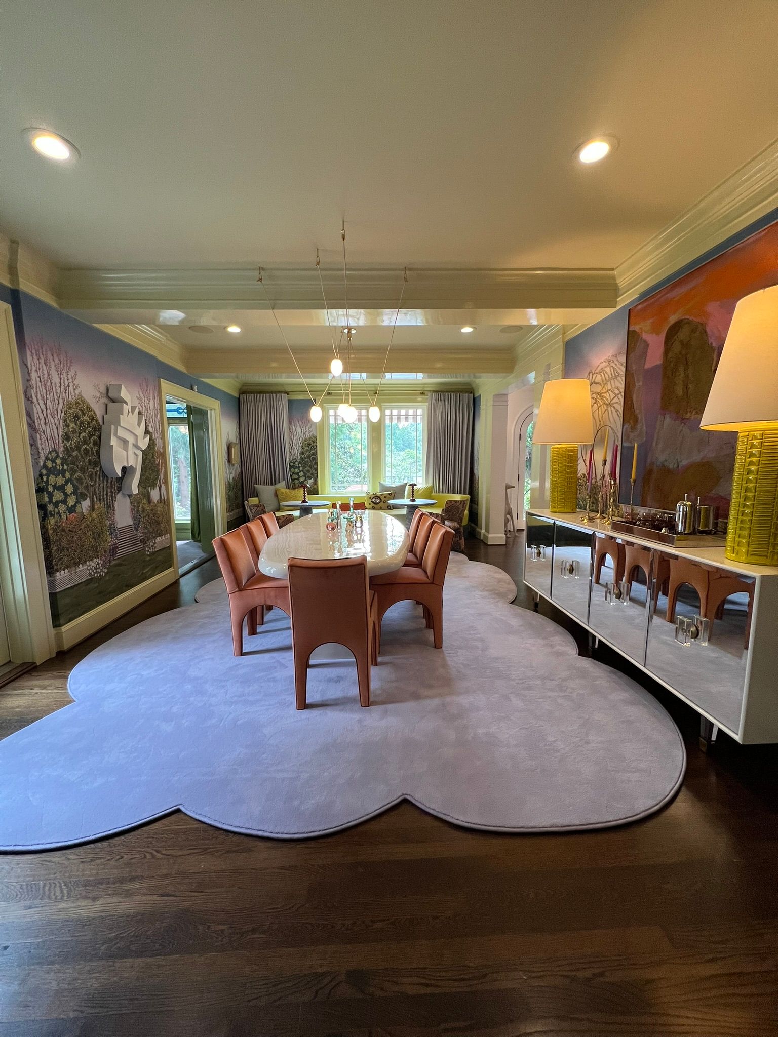 Elegant dining room with long table, chandelier, patterned walls, and a blue scalloped area rug