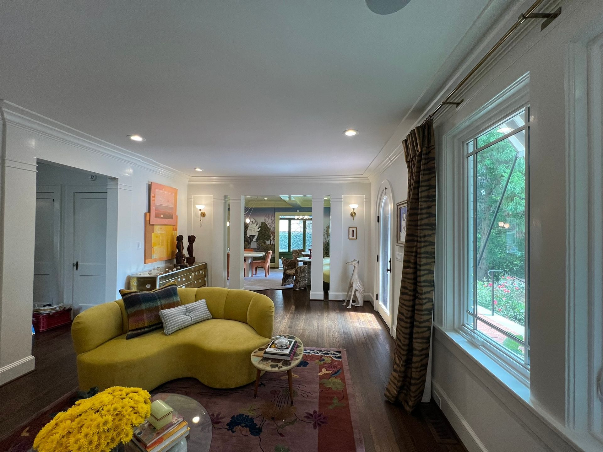 Bright living room with yellow curved sofa, large windows, and view to a dining area and garden.