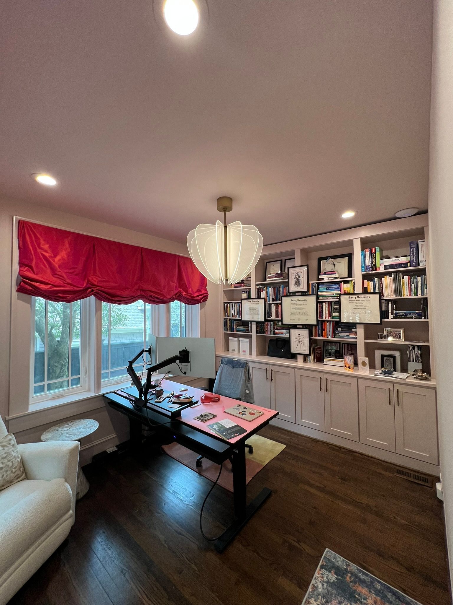 Home office with black desk, white built-ins, red curtains, and a large window overlooking trees