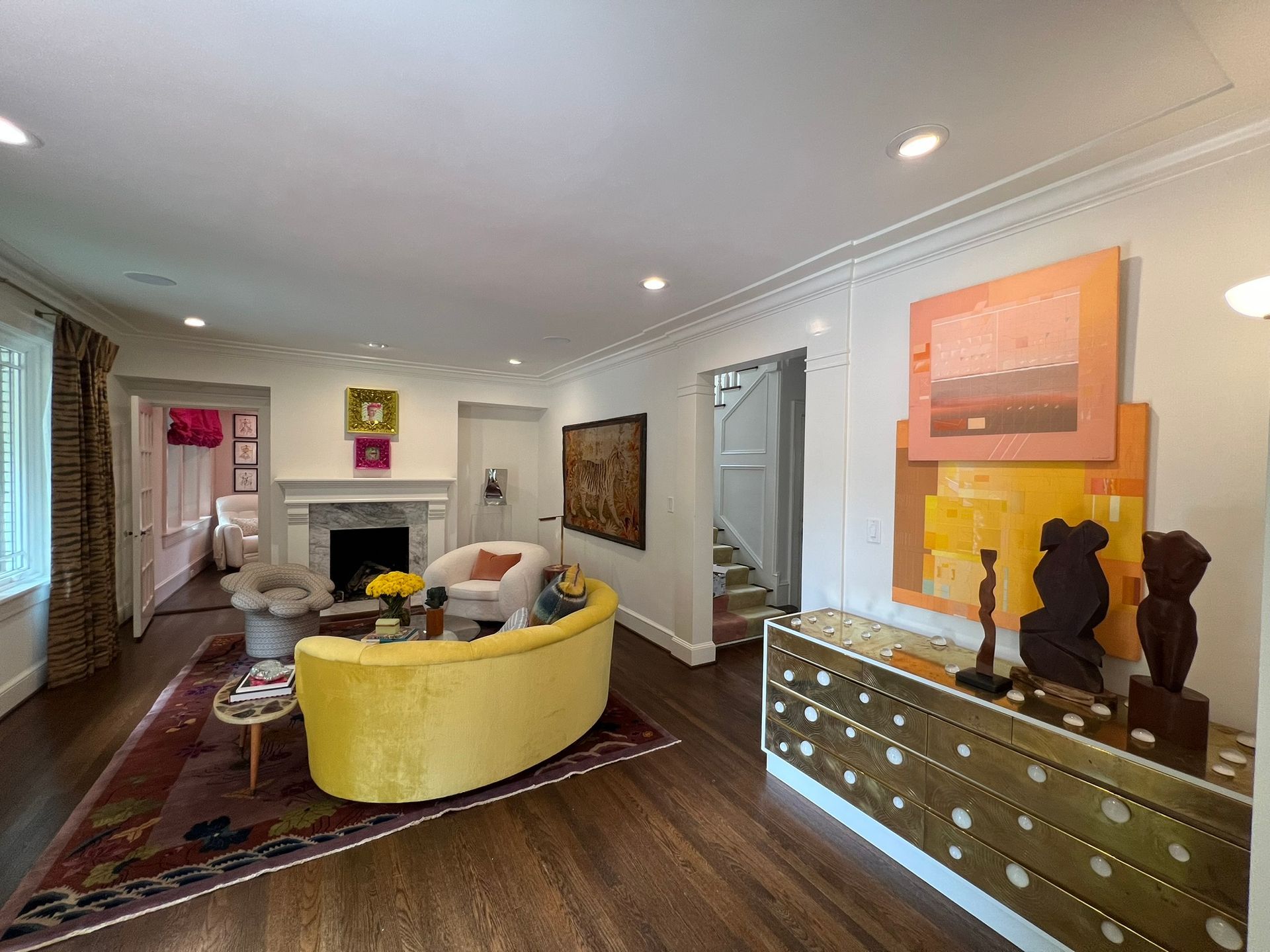 Bright living room with yellow chair, fireplace, mirror, artwork, and mirrored console table