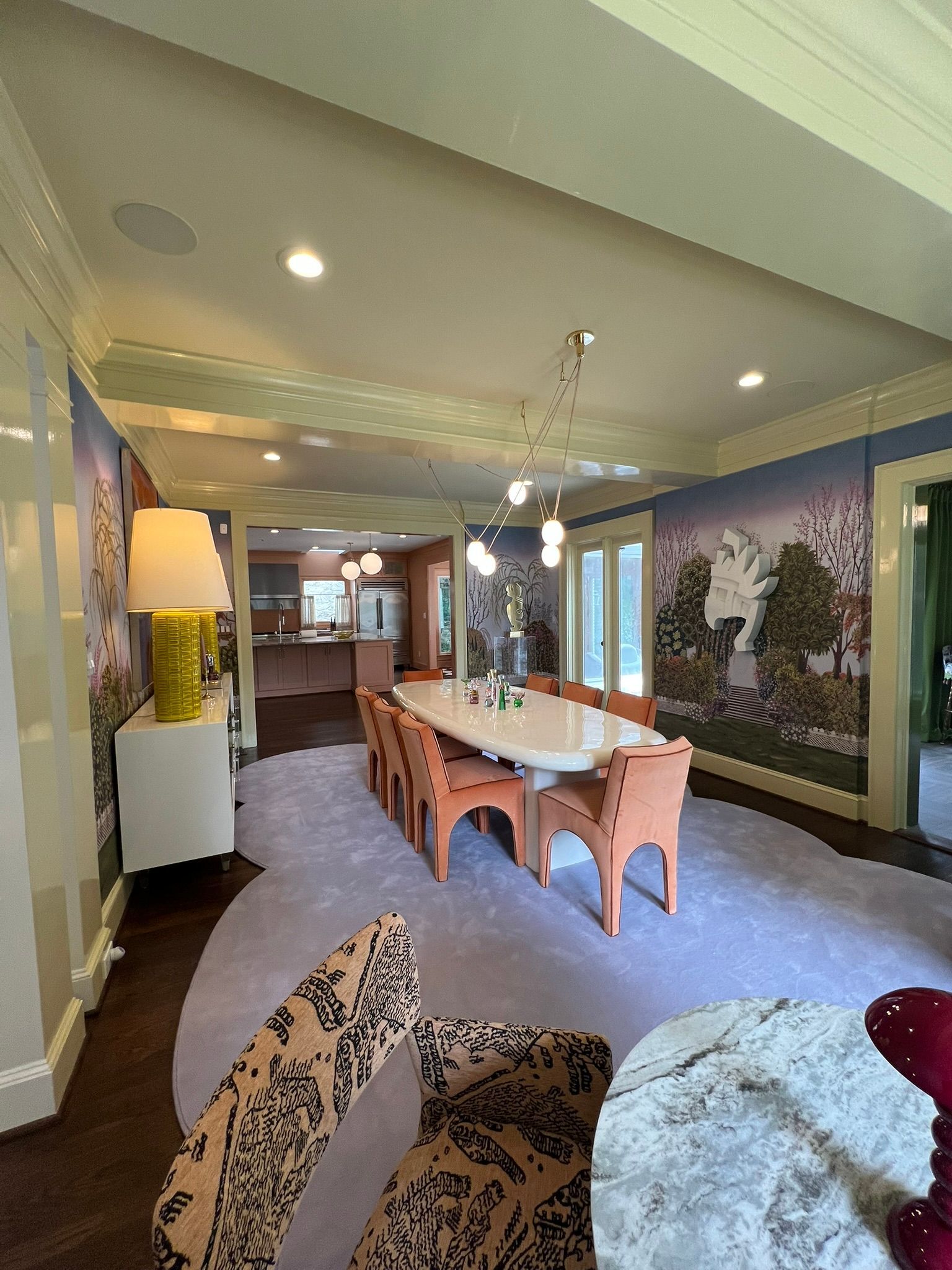 Elegant dining room with long wooden table, patterned wallpaper, recessed lights, and large windows