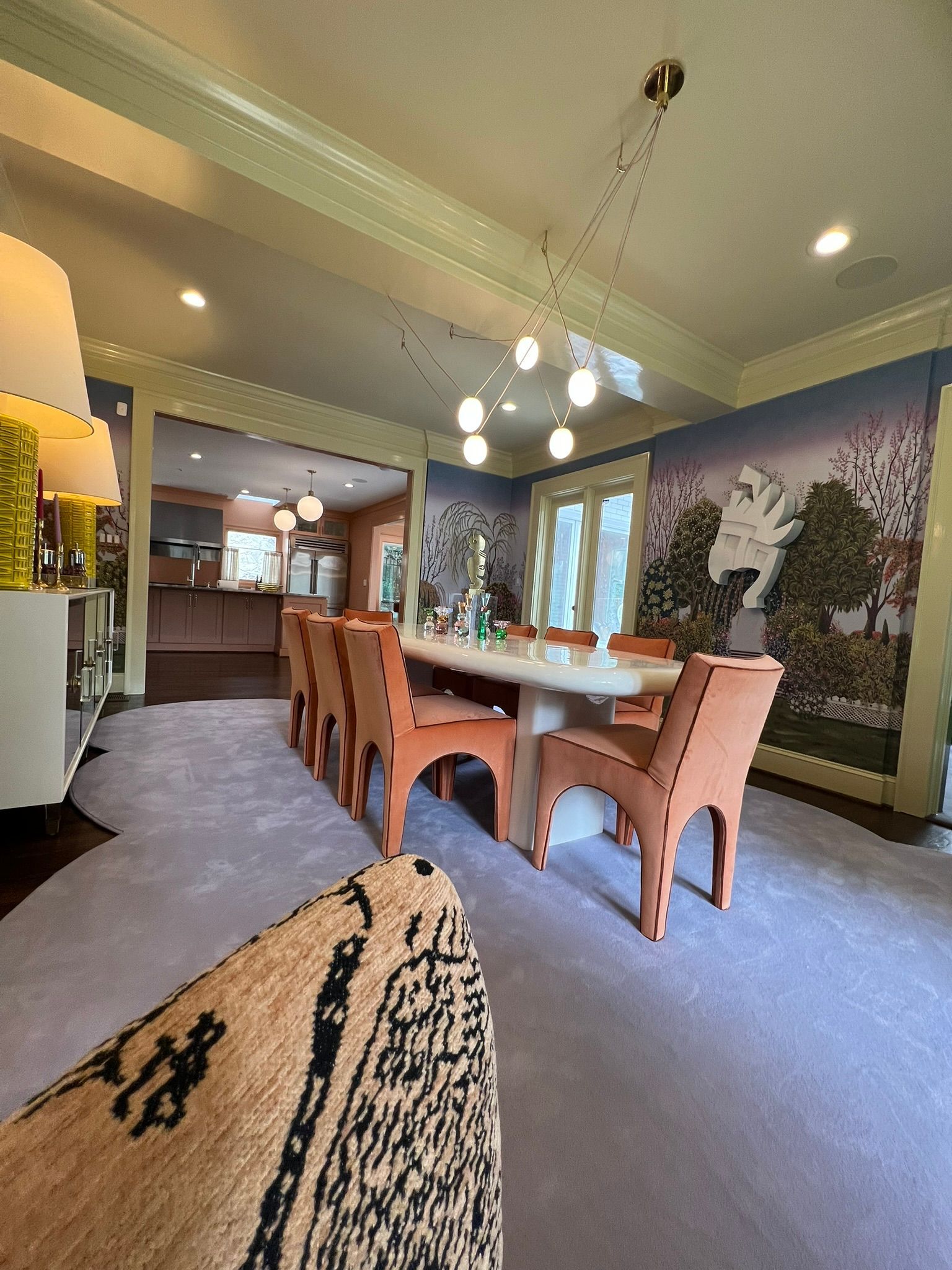 Dining room with long wooden table, pink chairs, mural wall art, and large windows