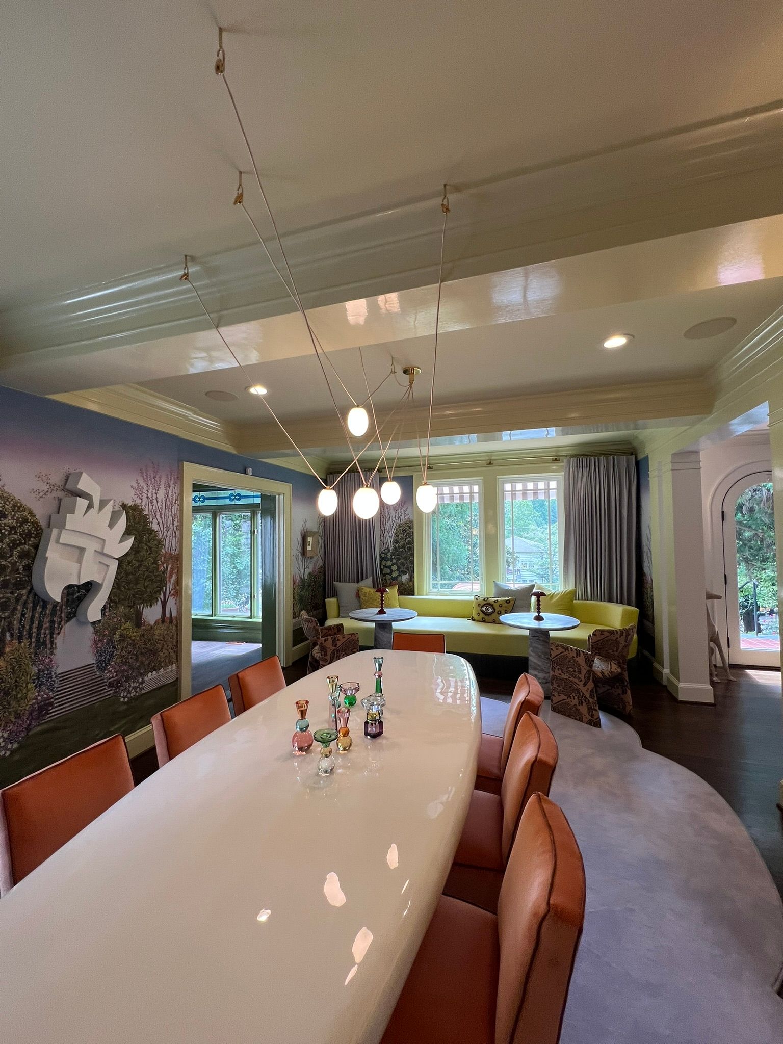 Modern dining room with long white table, tan chairs, pendant lights, and large windows overlooking greenery