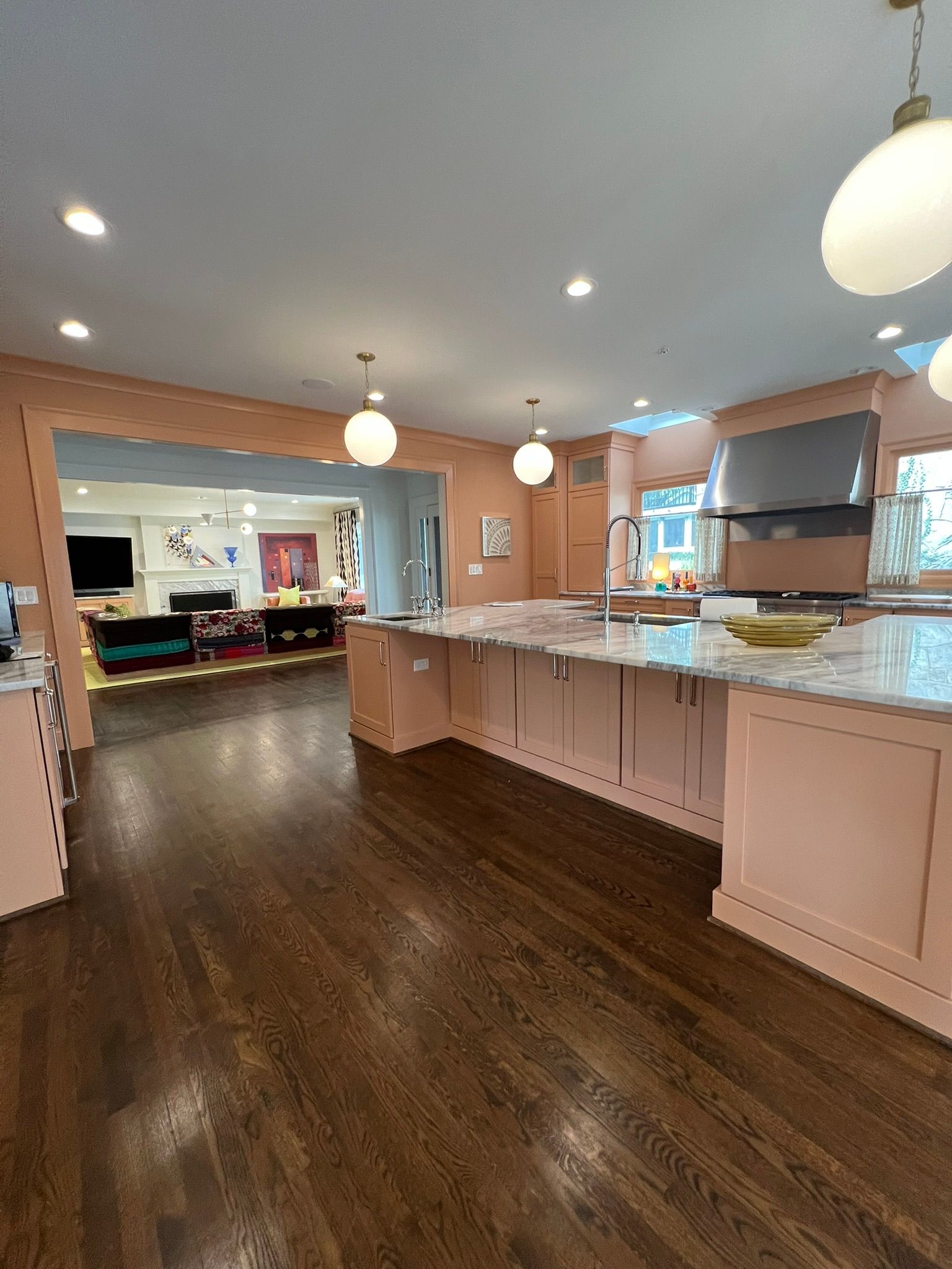 Spacious kitchen with pink cabinets, dark wood floors, white island, and pendant lights