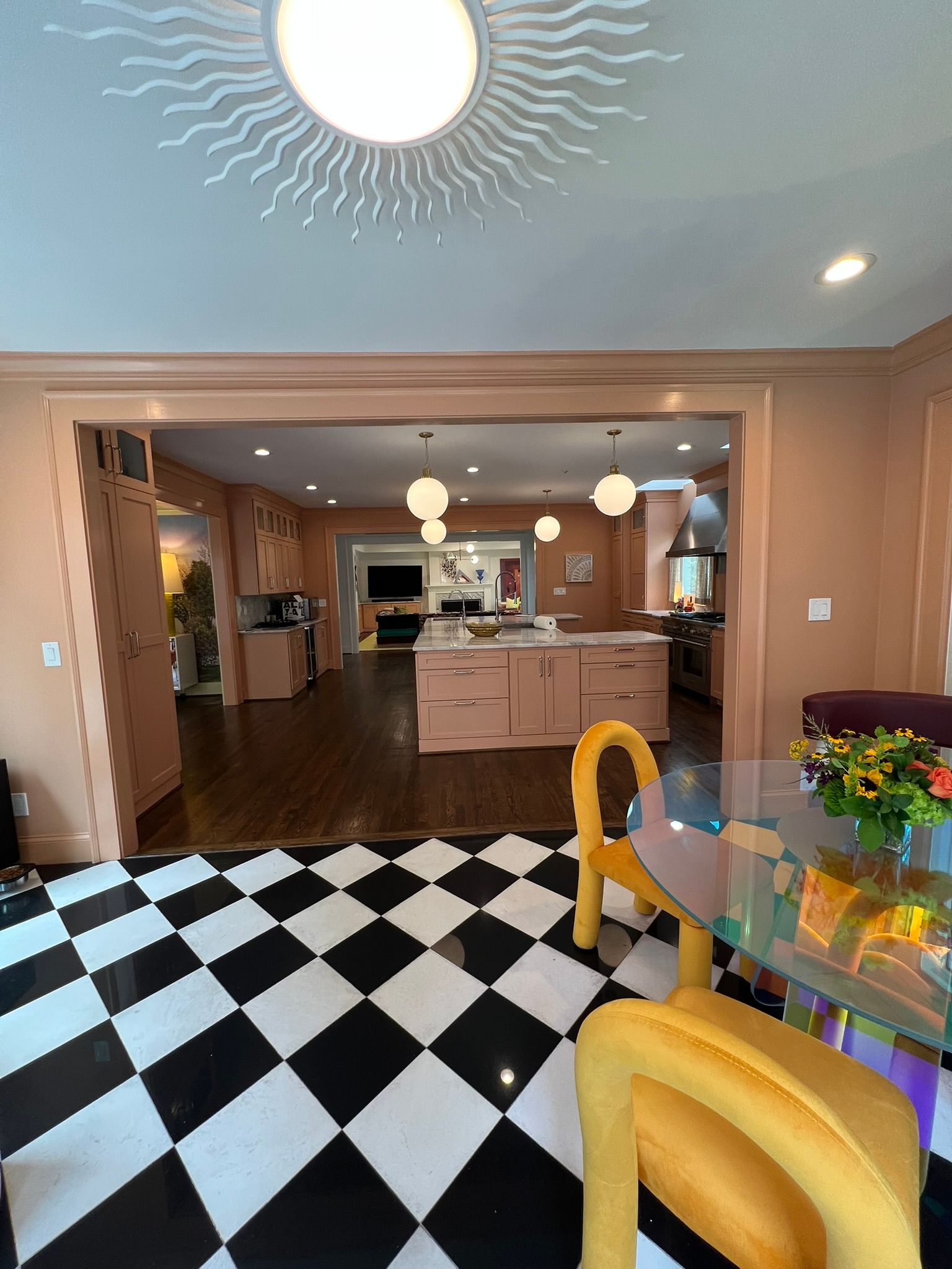 Bright kitchen and dining area with black-and-white checkered floor, yellow chairs, and pink island cabinets