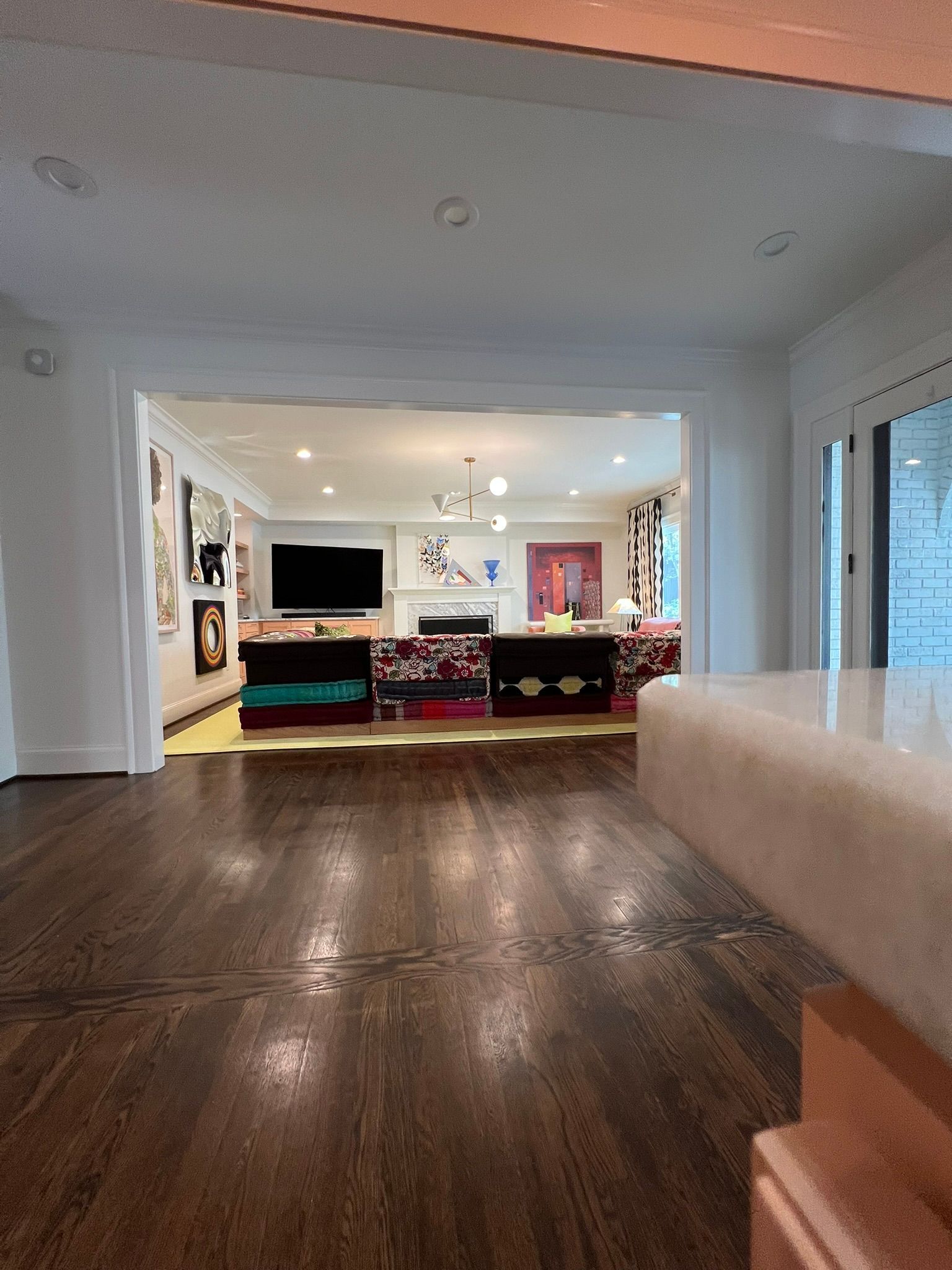 Open living room with dark wood floors, white trim, and a view into a colorful family room beyond.