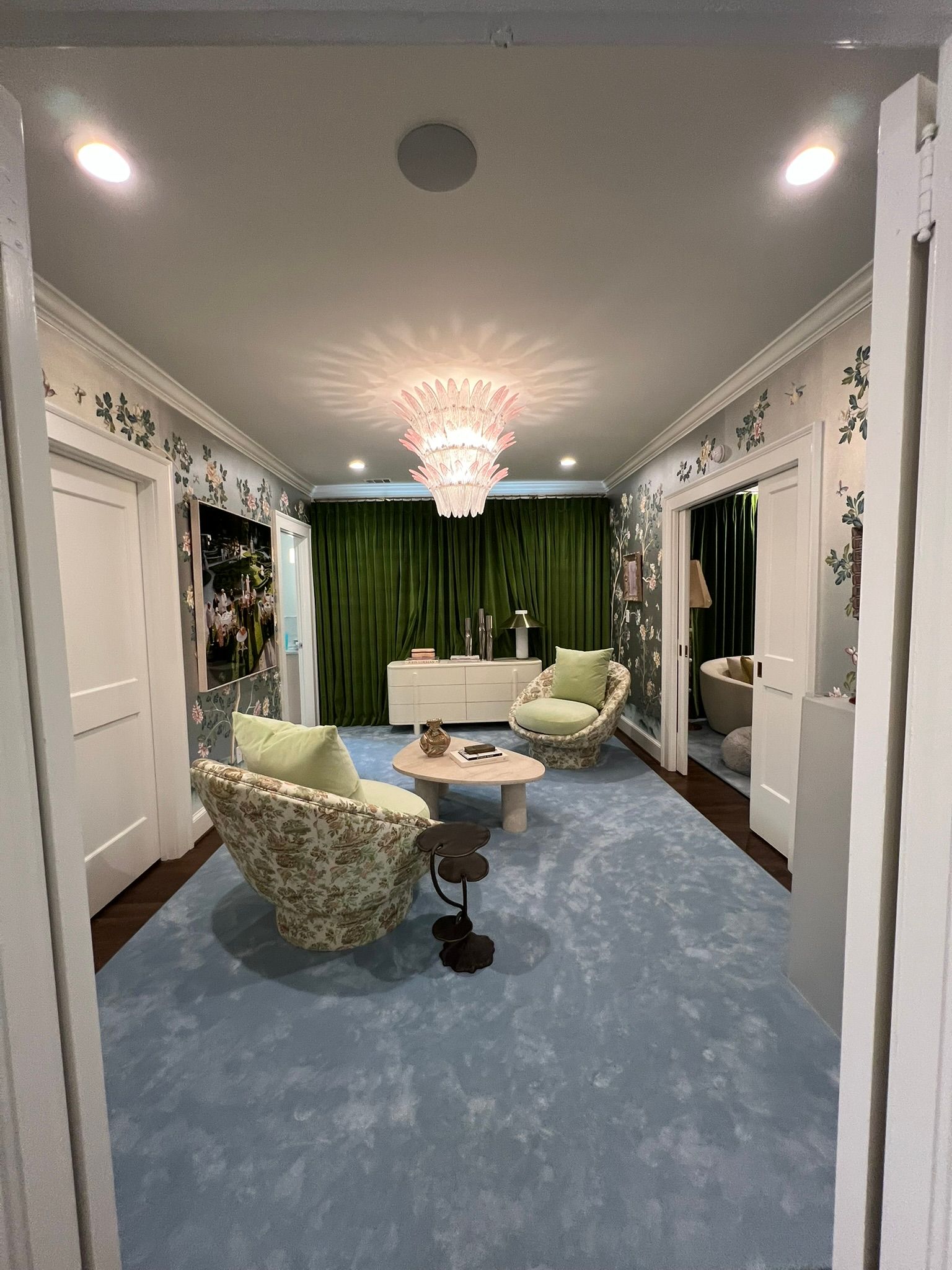 Stylish living room with blue carpet, green curtains, white walls, and modern seating under a chandelier