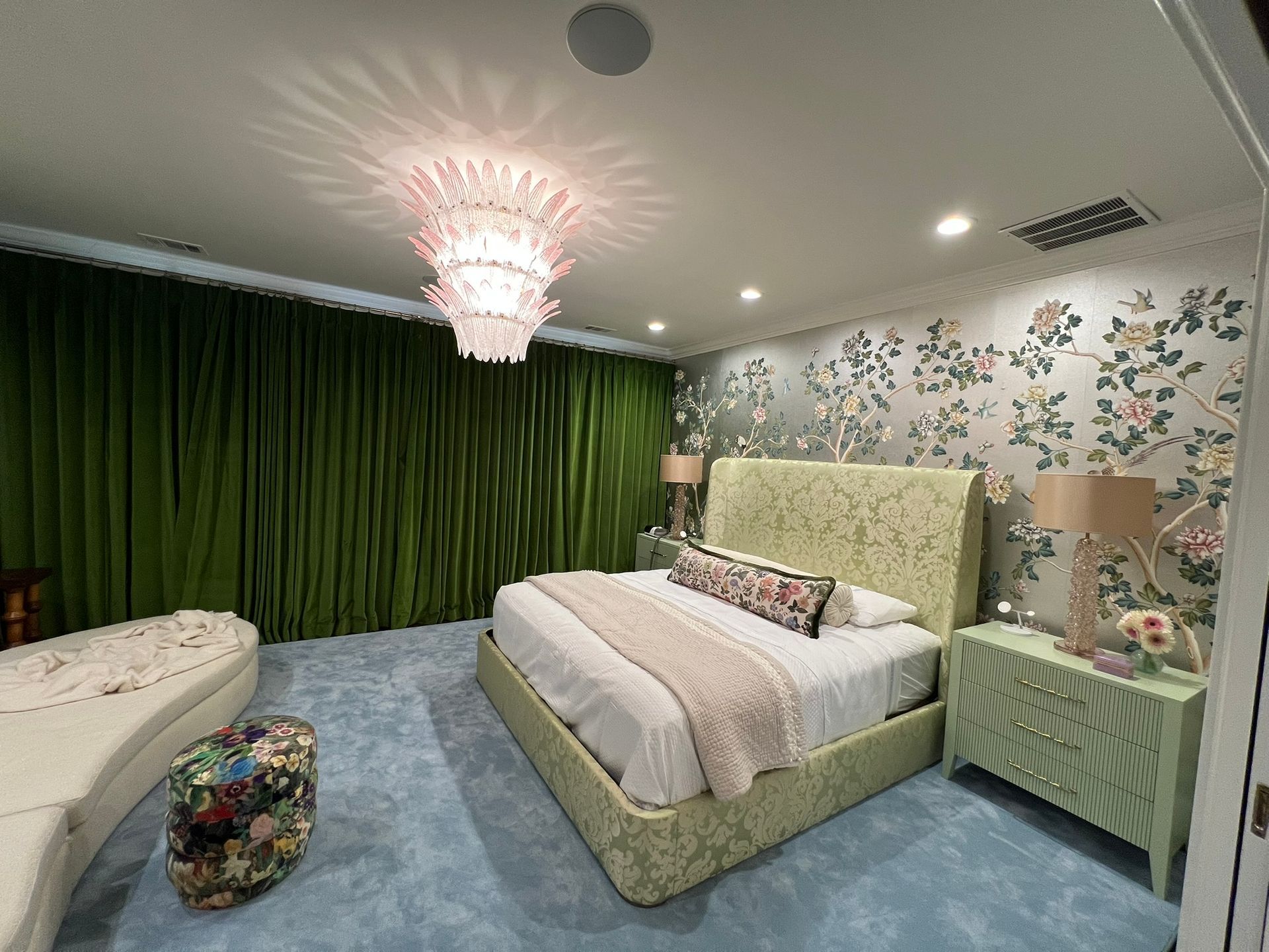Bedroom with green curtains, floral wallpaper, pale bedspread, and a pink chandelier on the ceiling.