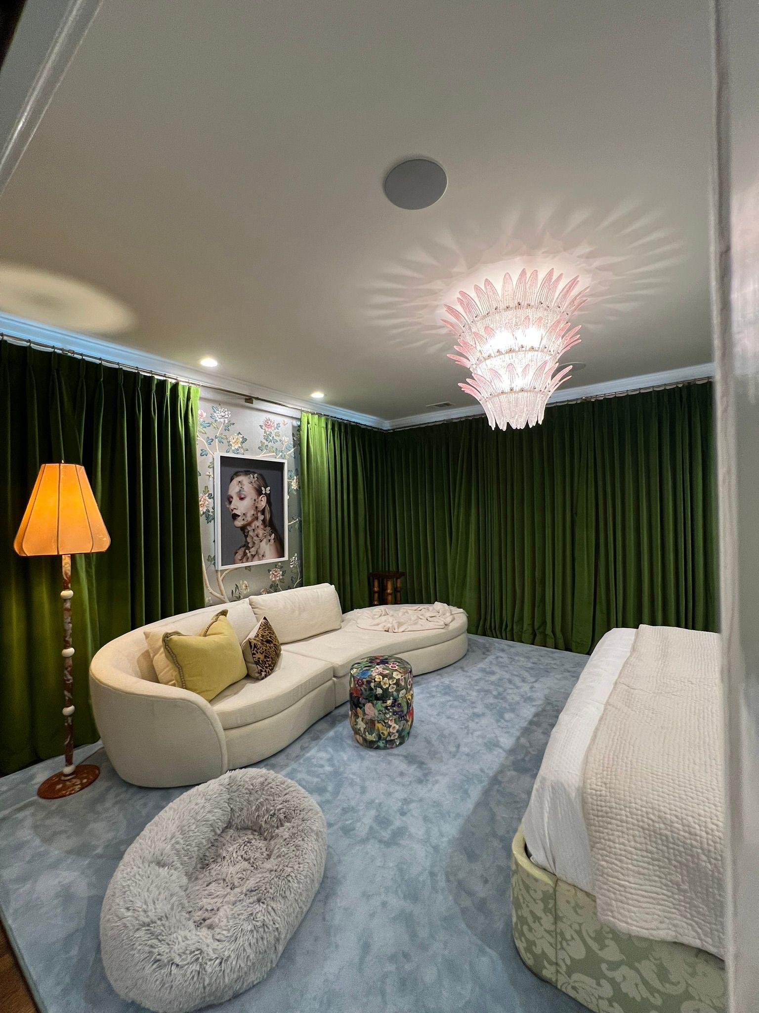 Elegant bedroom with green curtains, cream sofa bed, chandelier, floor lamp, and blue rug.