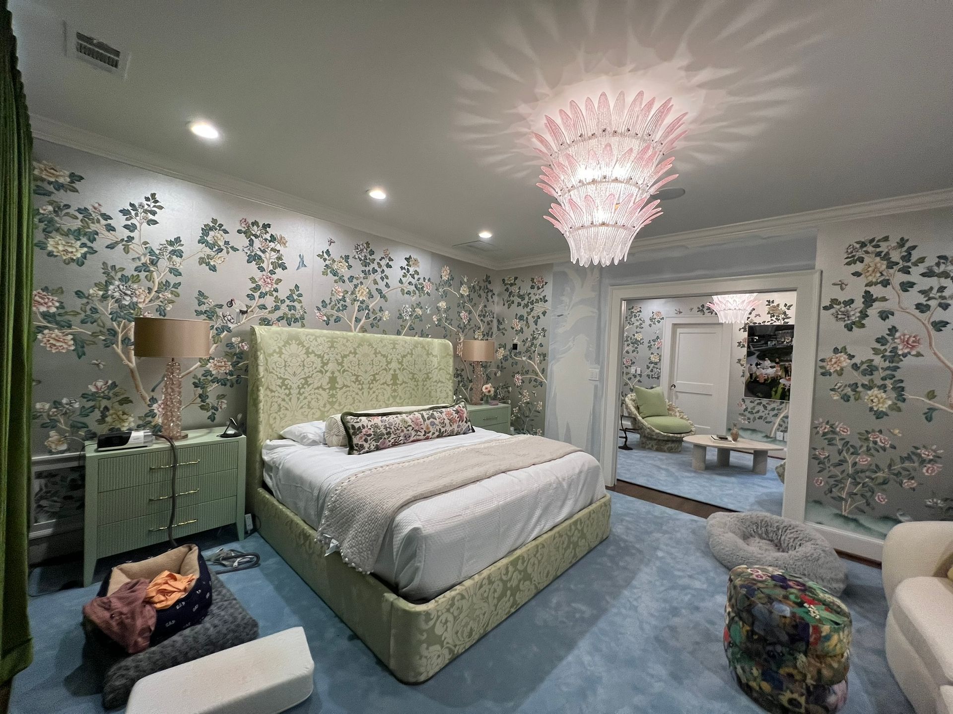 Floral bedroom with a green bed, blue carpet, mirrored wall, and pink chandelier.