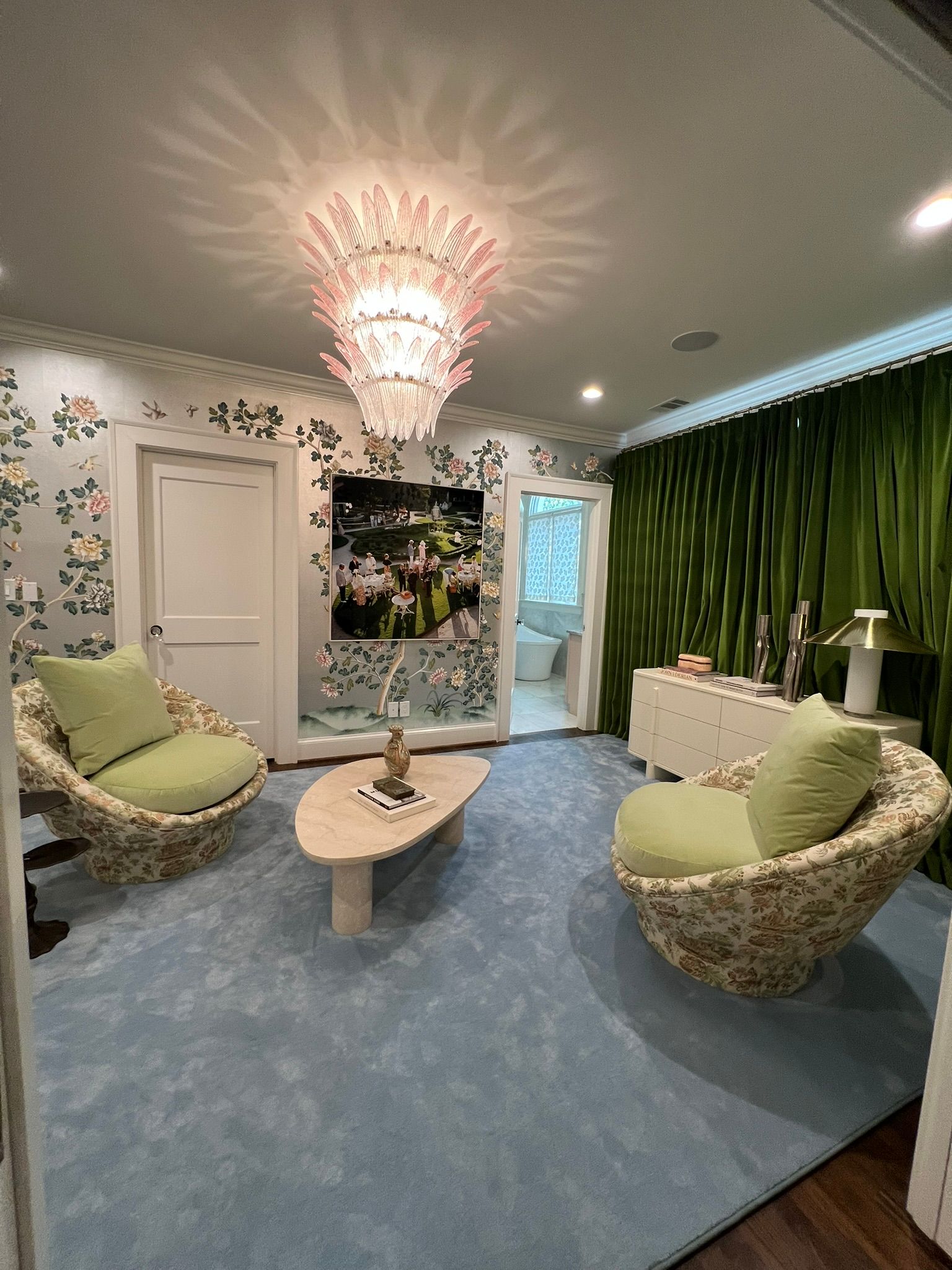 Cozy living room with blue carpet, green chairs, chandelier, and tall green curtains.