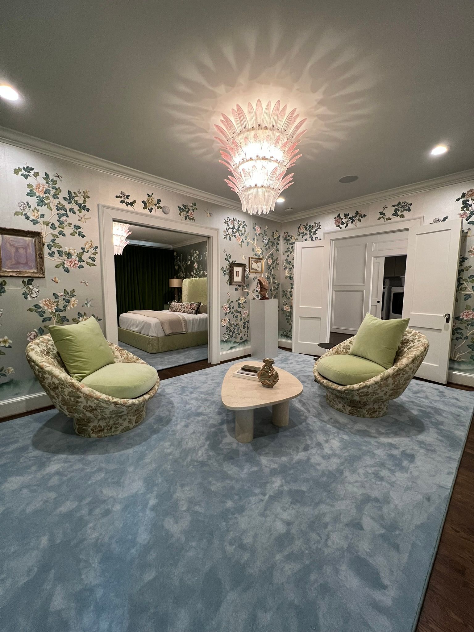 Elegant bedroom sitting area with blue carpet, green chairs, mirrored wall, and chandelier lighting