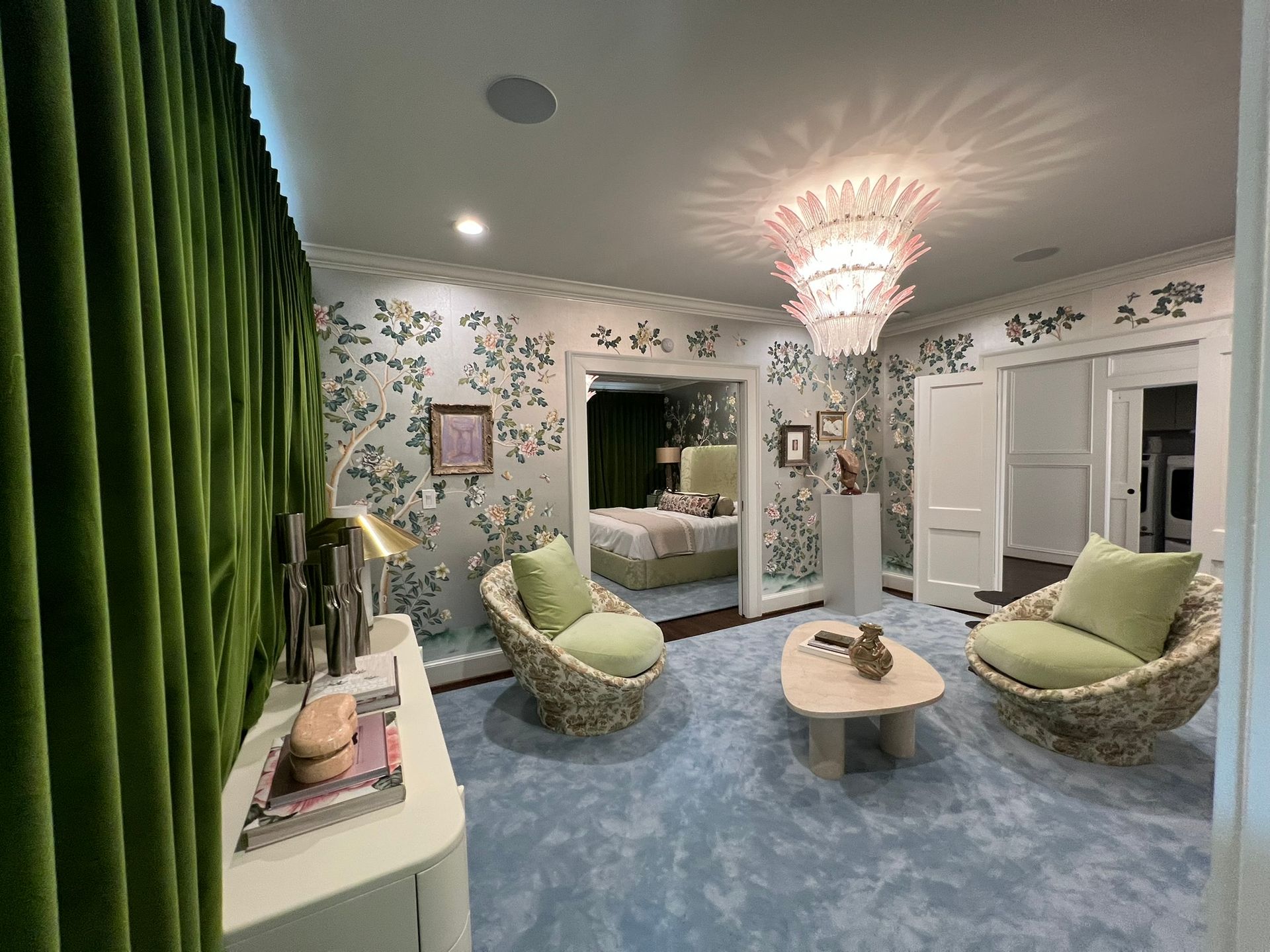 Pastel bedroom sitting area with green chairs, floral wallpaper, blue carpet, and chandelier