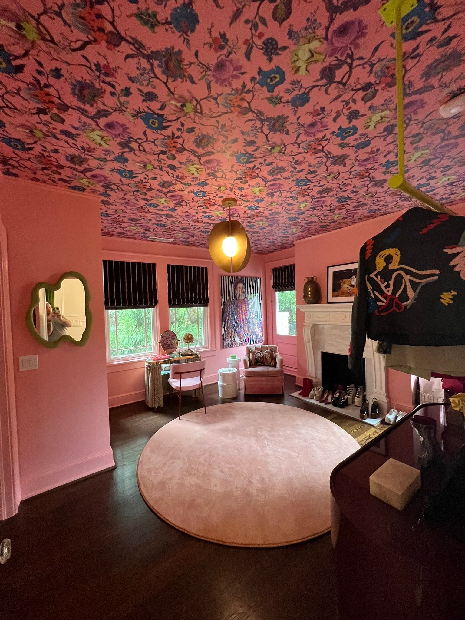 Pink room with floral ceiling, round rug, hanging lamp, and seating by a window.