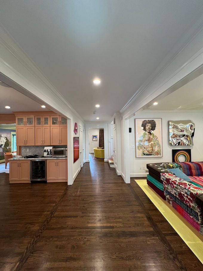 Long hallway with dark wood floors, recessed lights, kitchen on left, colorful couch and wall art on right.