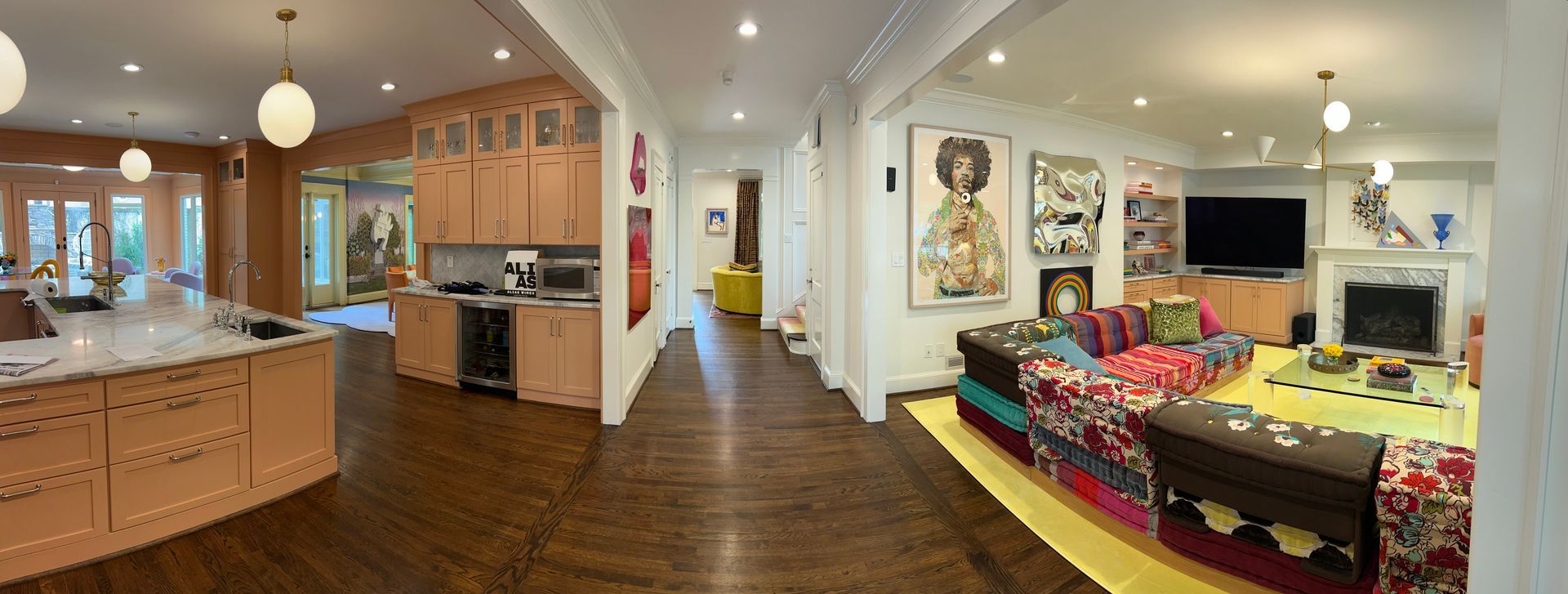 Open-concept kitchen and living room with wood cabinets, colorful sofa, and TV in a warmly lit home