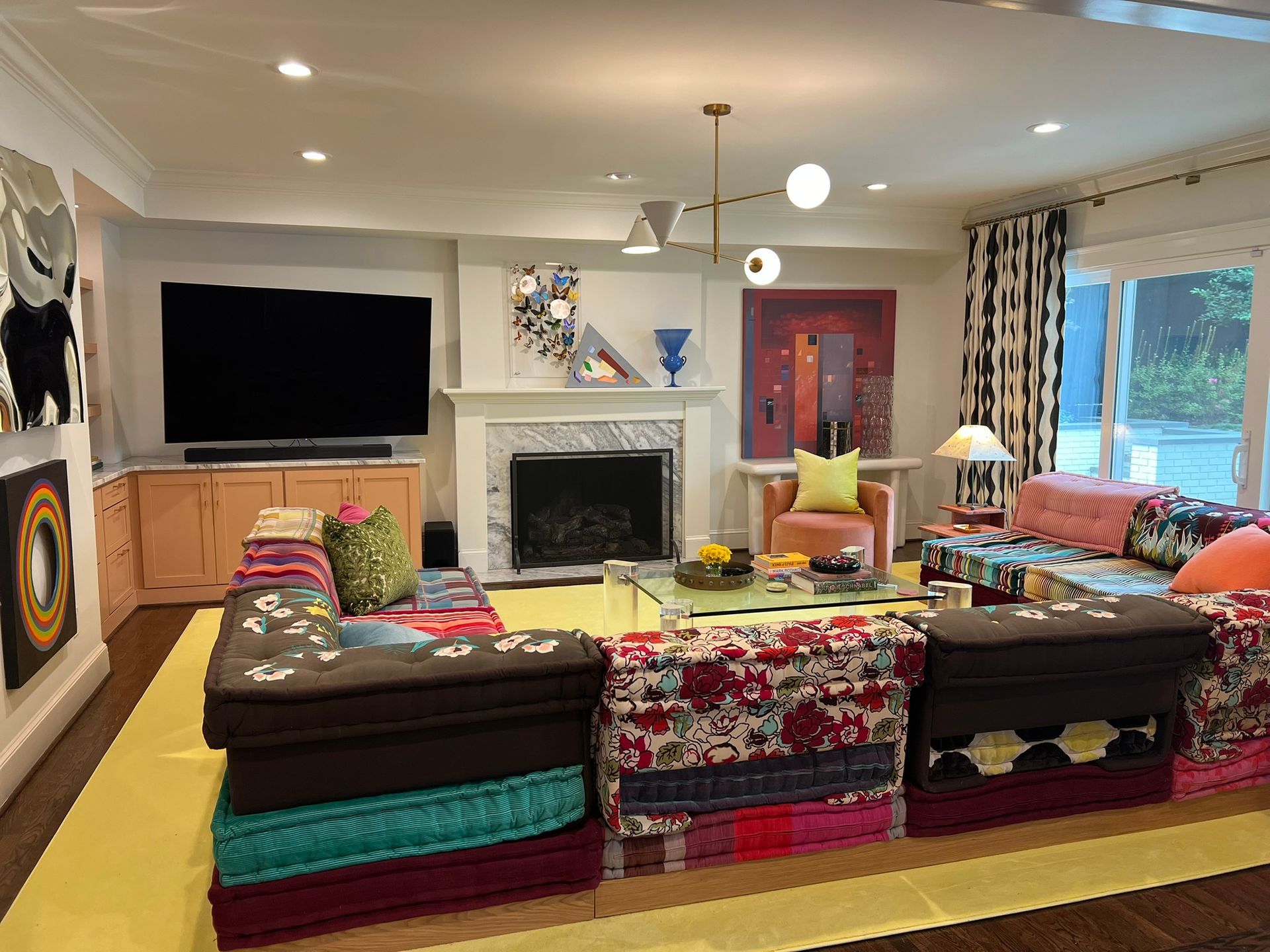Cozy living room with fireplace, large TV, colorful patterned sofas, and sliding glass door to a patio
