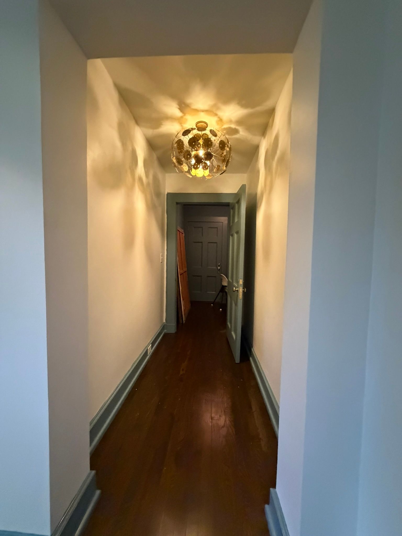 Narrow hallway with white walls, dark wood floor, and a glowing pendant light at the far end.