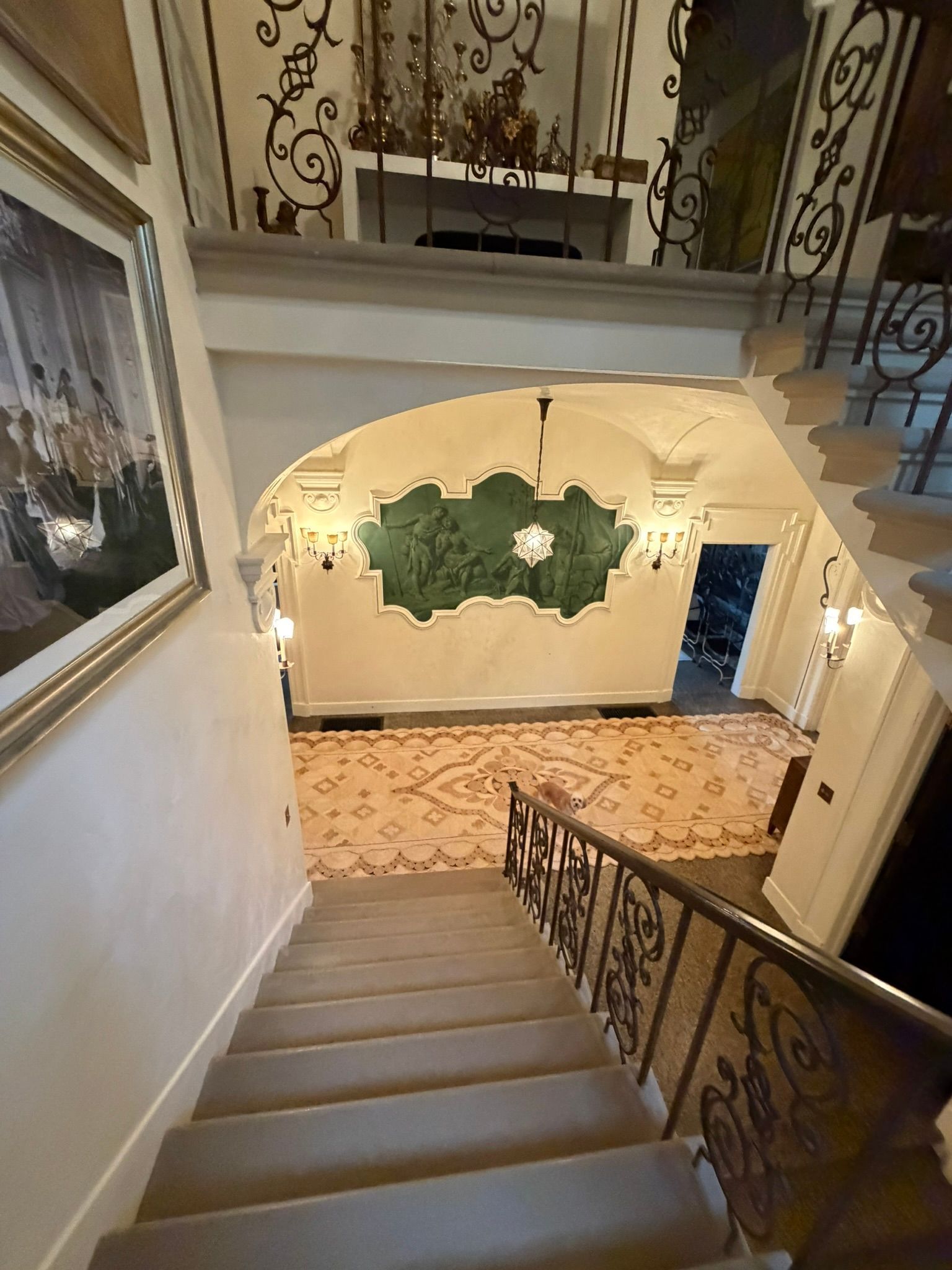Staircase in an elegant foyer with wrought-iron railings, a patterned tile floor, and arched wall decor.