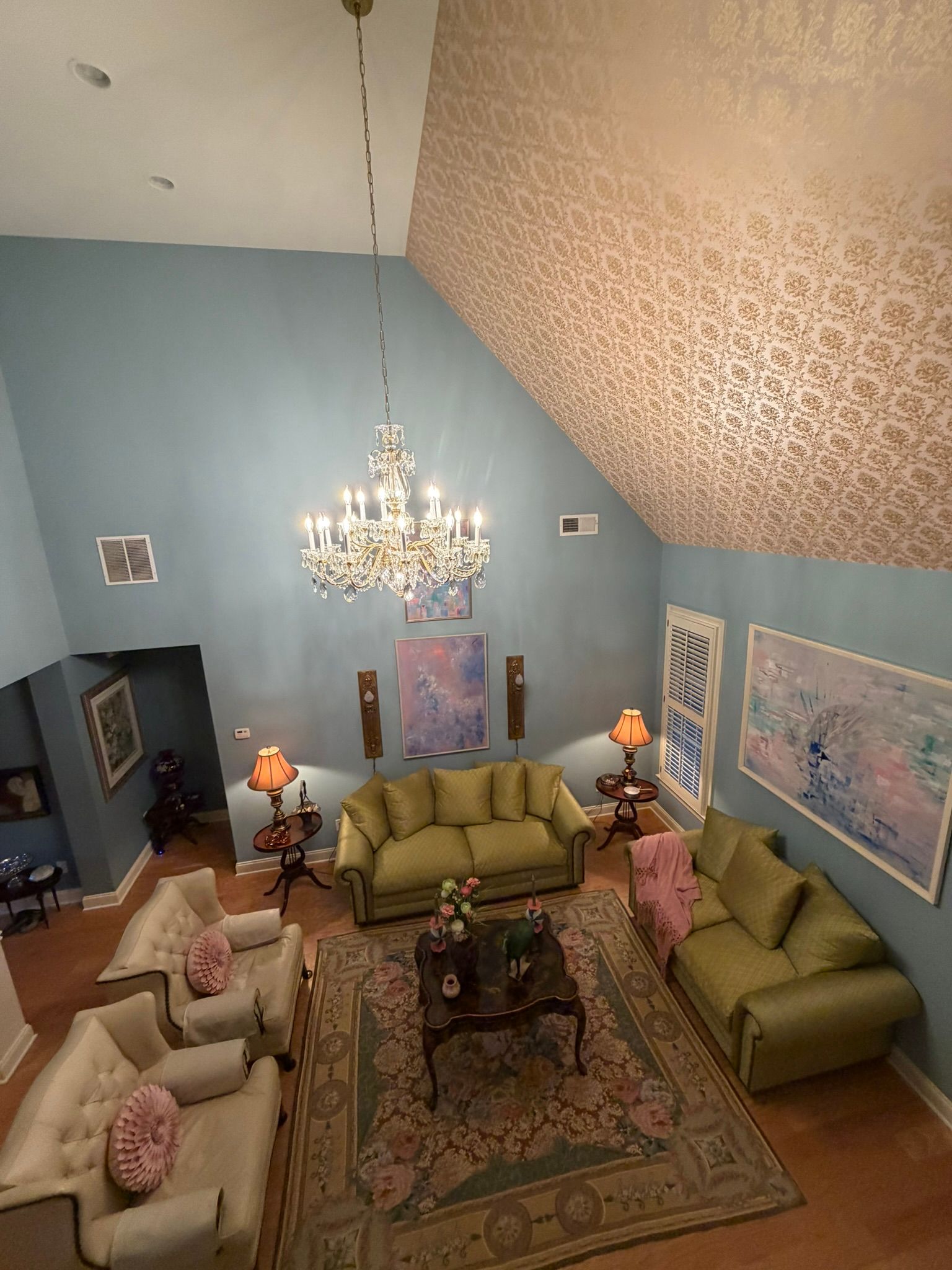 High-ceiling living room with blue walls, chandeliers, sofas, and a large rug