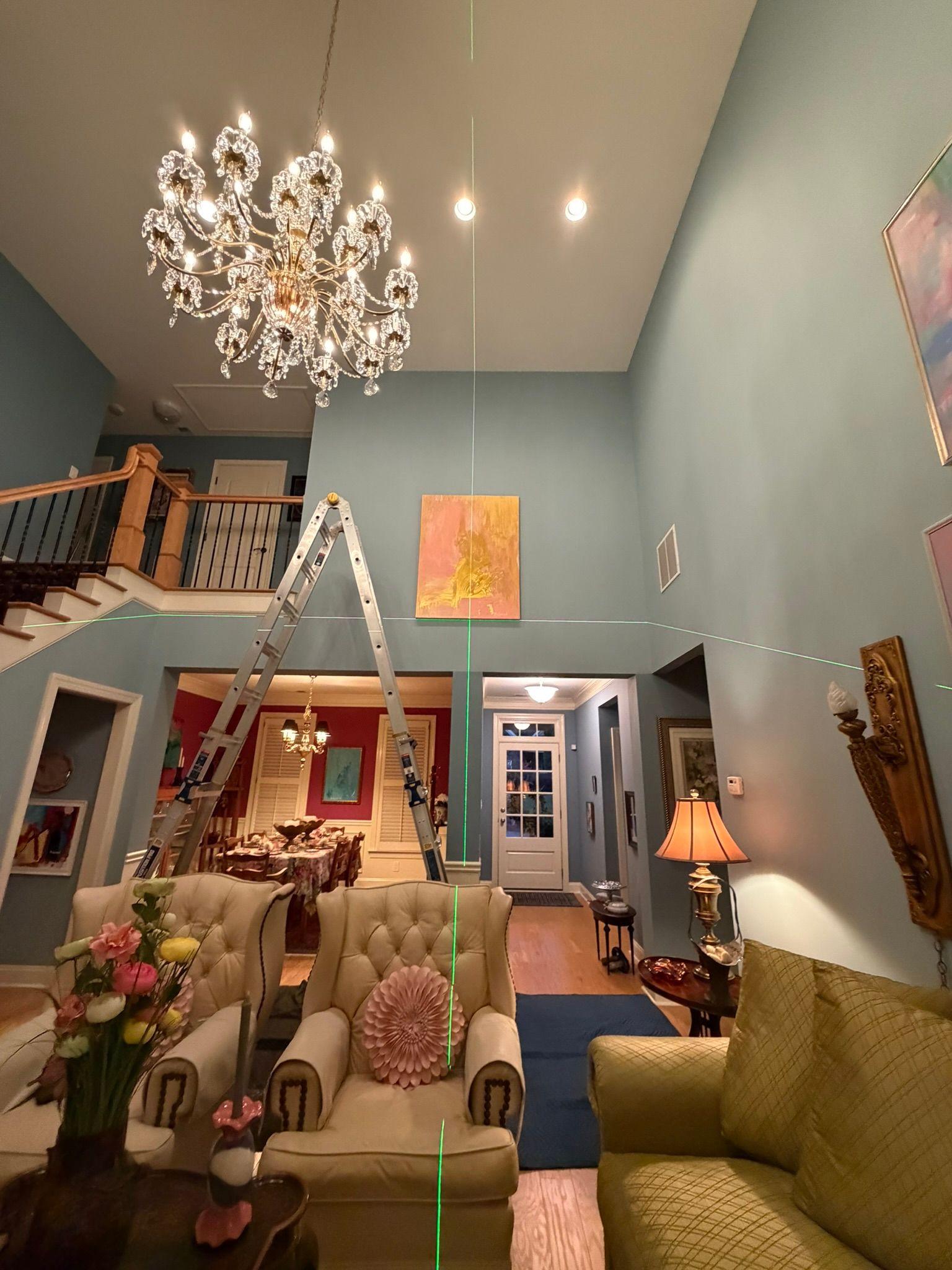 Elegant living room with high ceiling, chandelier, staircase, sofas, and soft blue walls