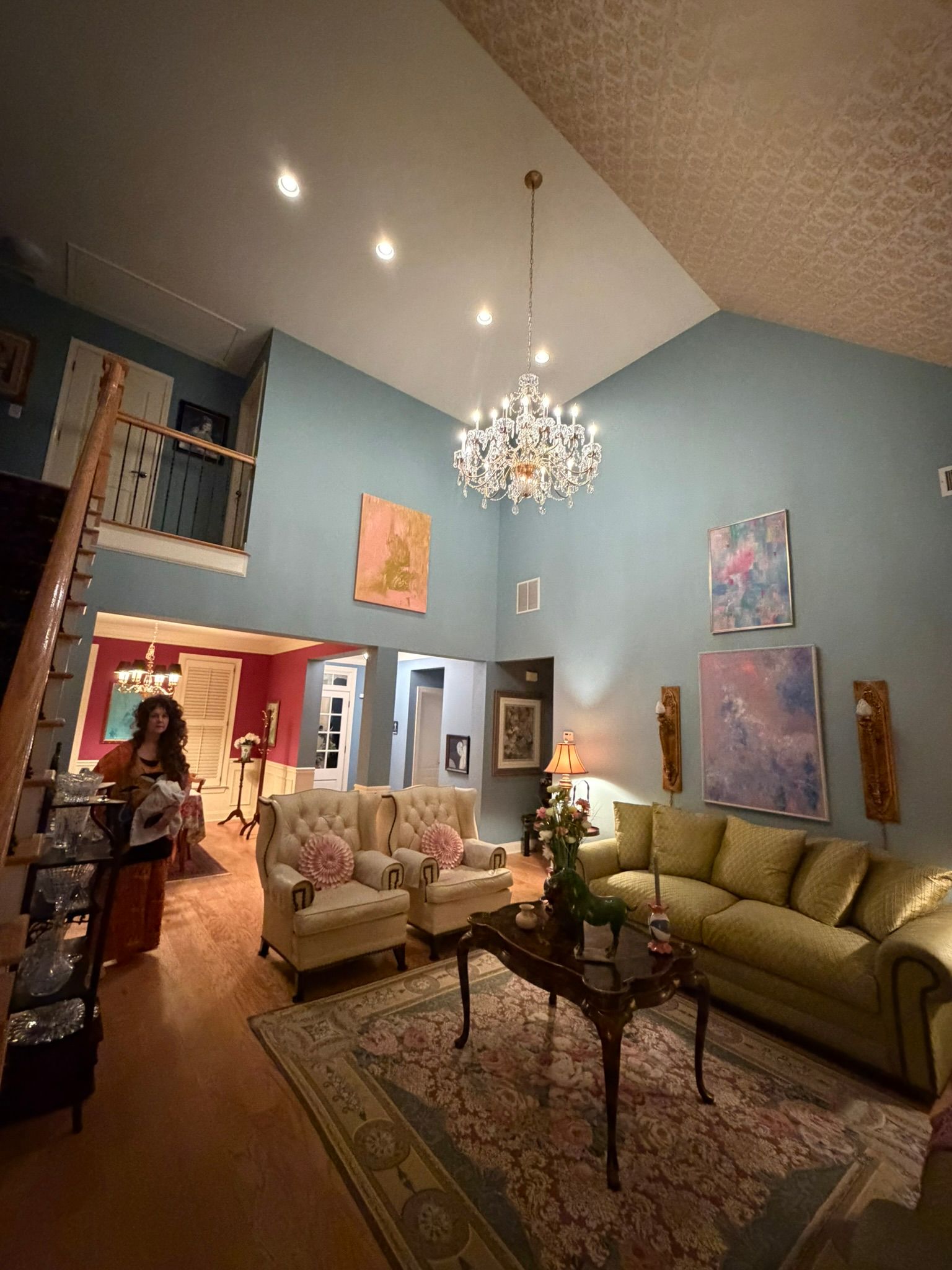 Elegant blue living room with chandelier, green sofa, patterned rug, and staircase loft.