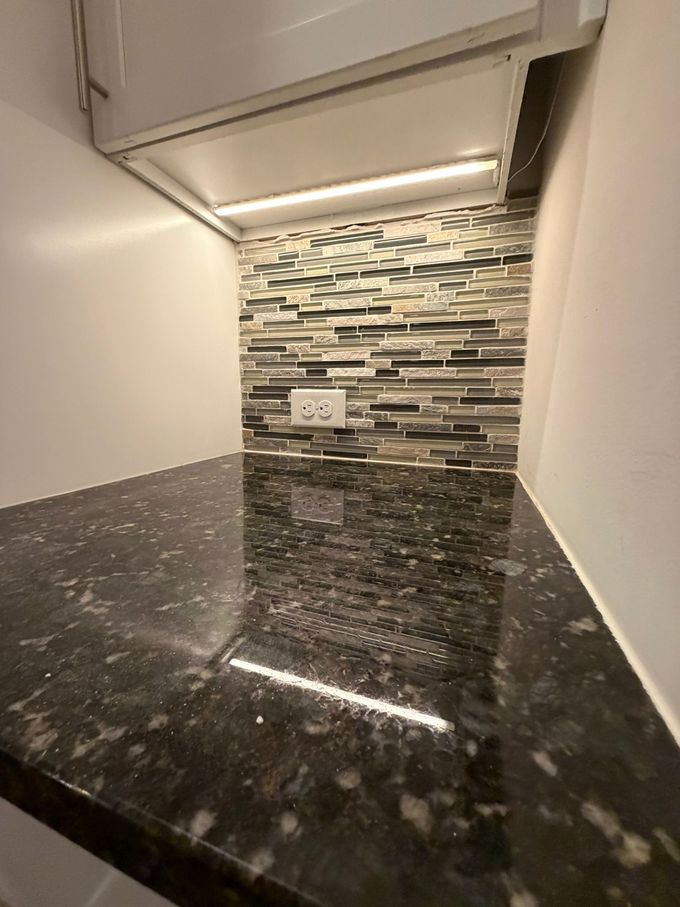 Black granite countertop in a kitchen with white cabinets and a mosaic tile backsplash.