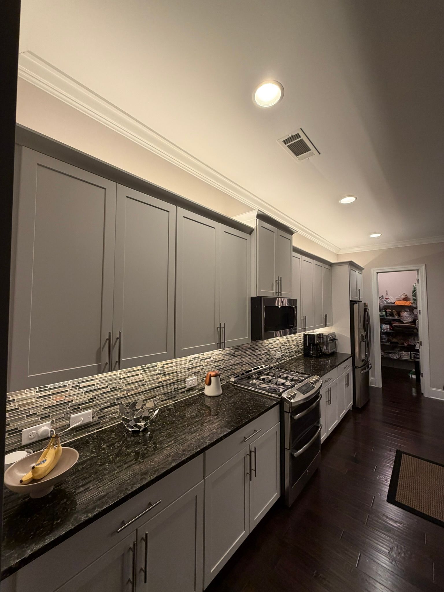 Modern kitchen with gray cabinets, dark countertops, mosaic backsplash, and recessed ceiling lights