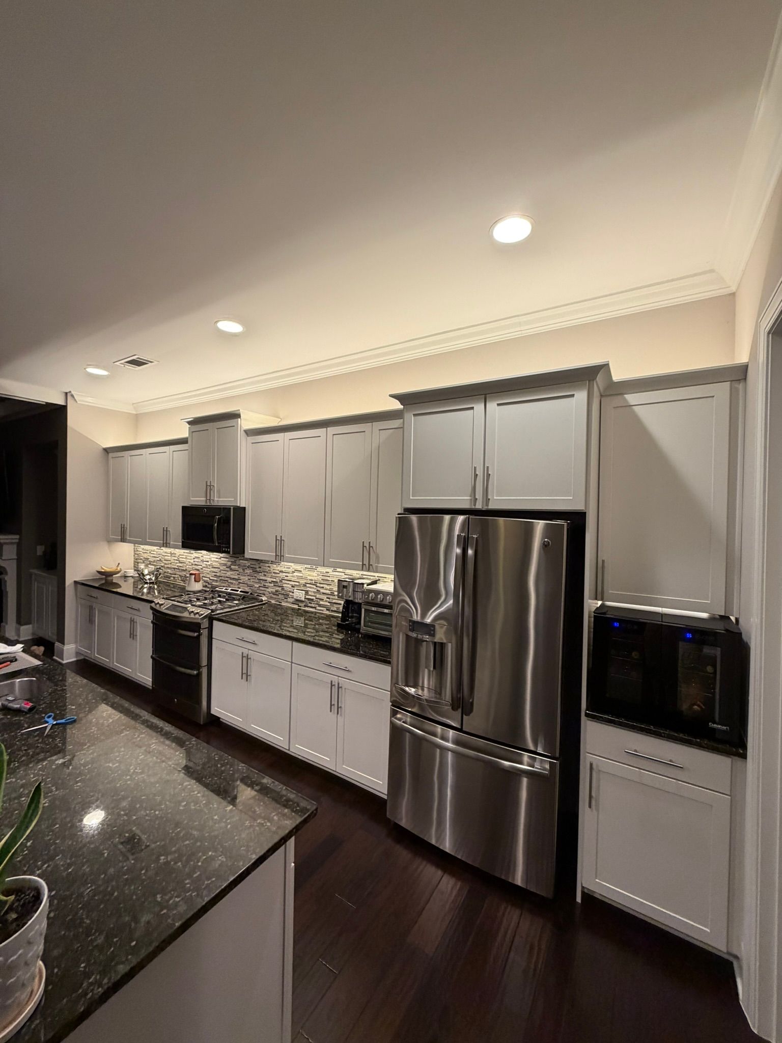 Bright modern kitchen with white cabinets, stainless steel fridge, and dark granite counters