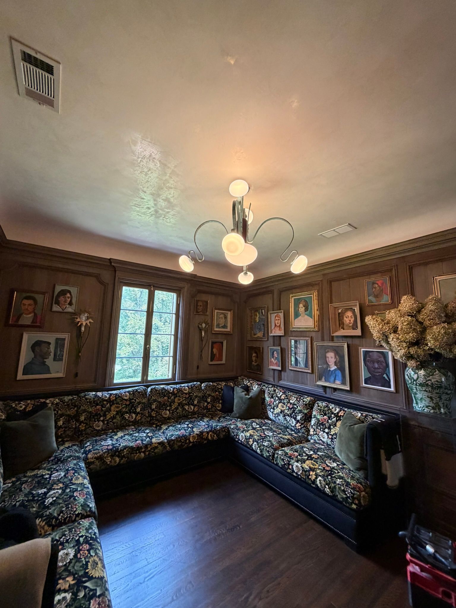 Cozy living room with patterned sectional sofa, framed art on wood-paneled walls, and a chandelier