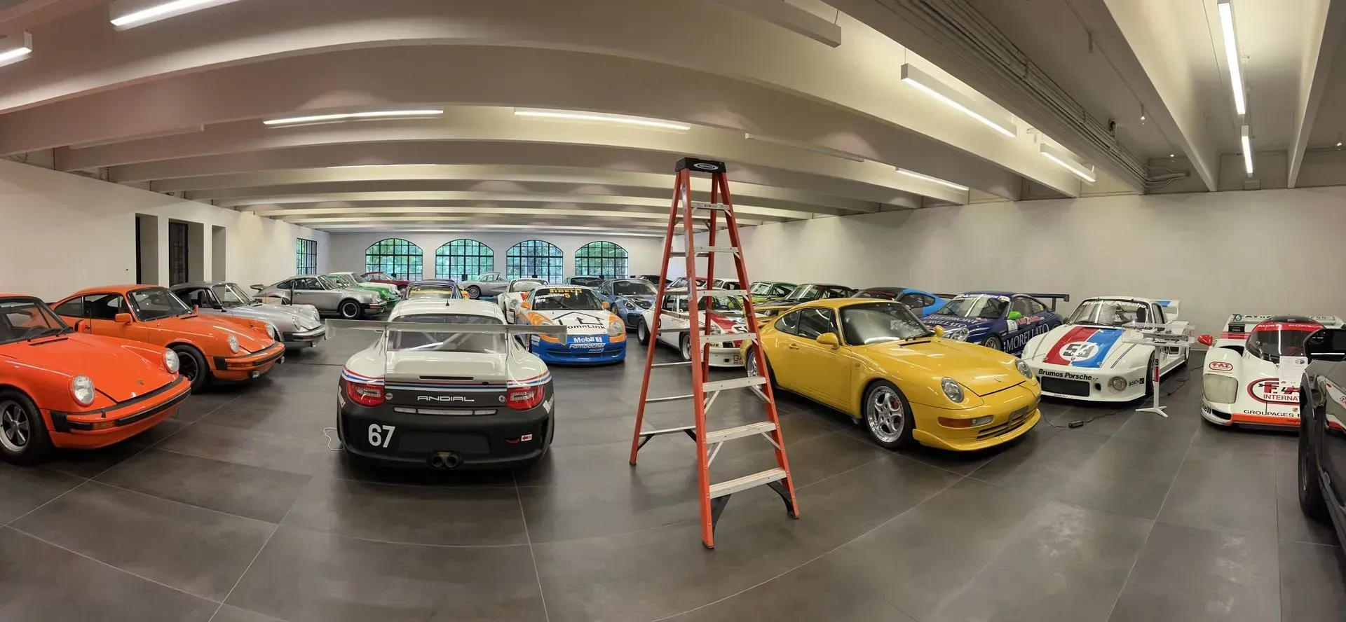 Classic cars displayed indoors, with a red ladder centered among the vehicles in a showroom.