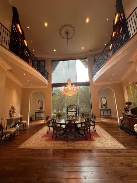 Elegant two-story foyer with wood floors, chandelier, grand staircase, and dining table by a large window