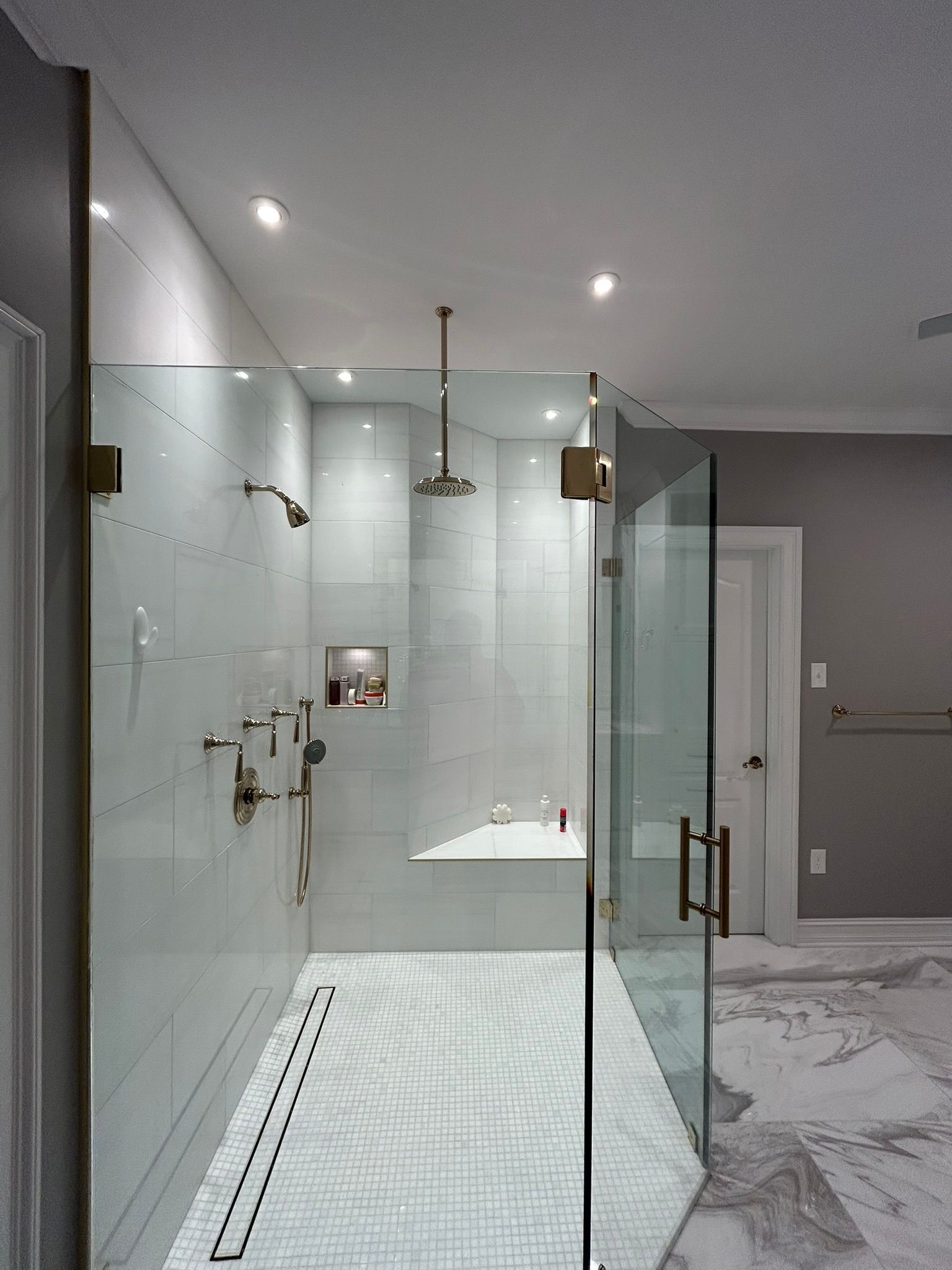 Modern glass-enclosed shower with white tile floor and gray bathroom walls