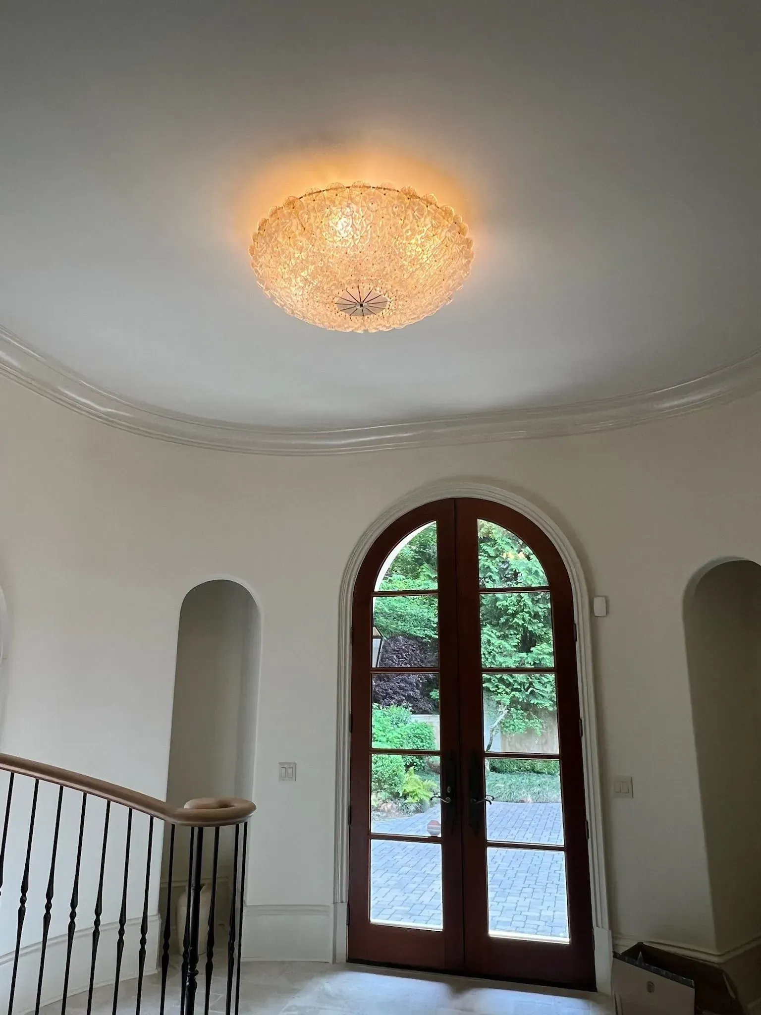 Elegant entryway with arched double doors, staircase railing, and a glowing ceiling light fixture