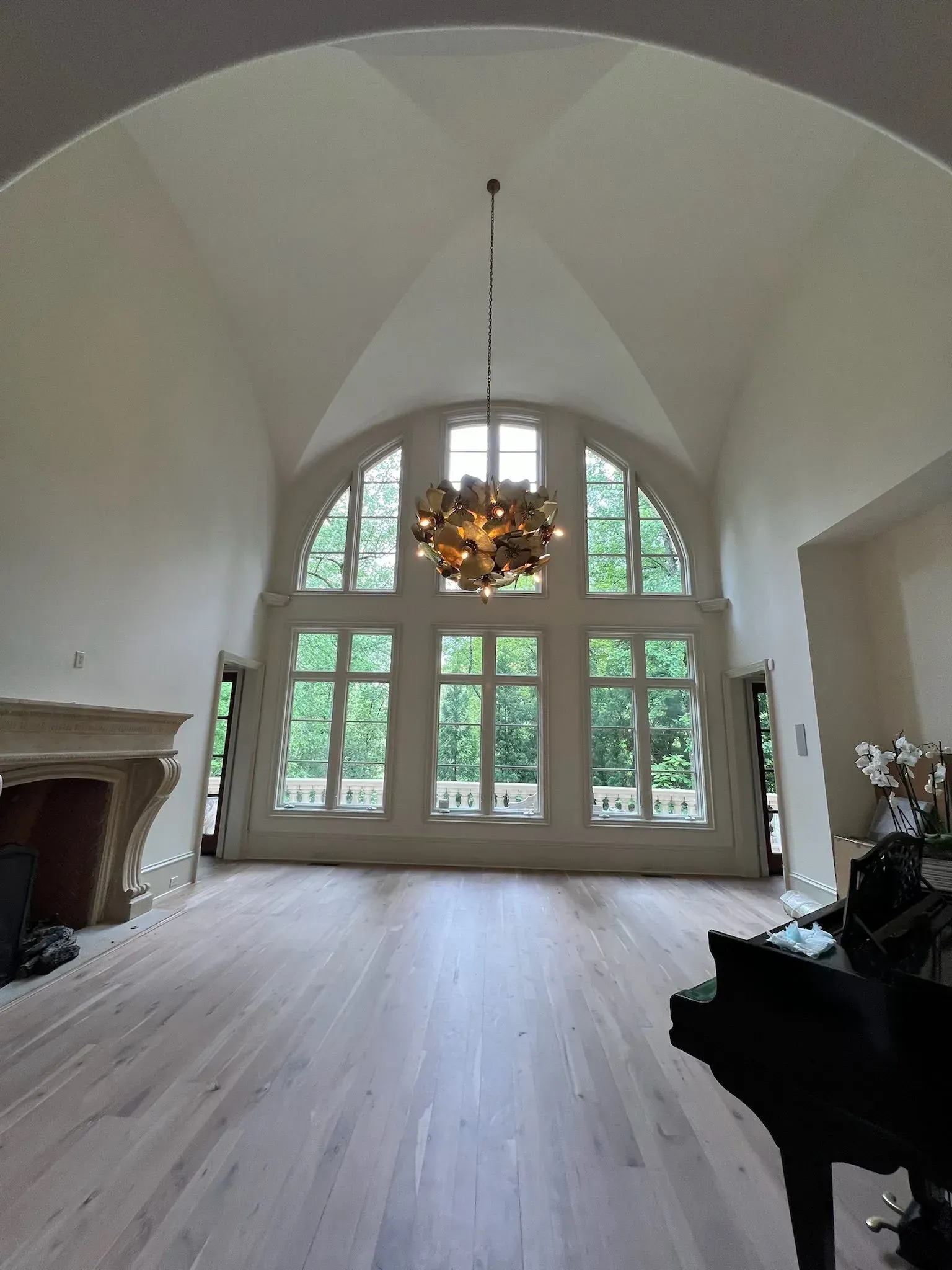 Elegant empty living room with vaulted ceiling, large arched windows, chandelier, and light wood floors