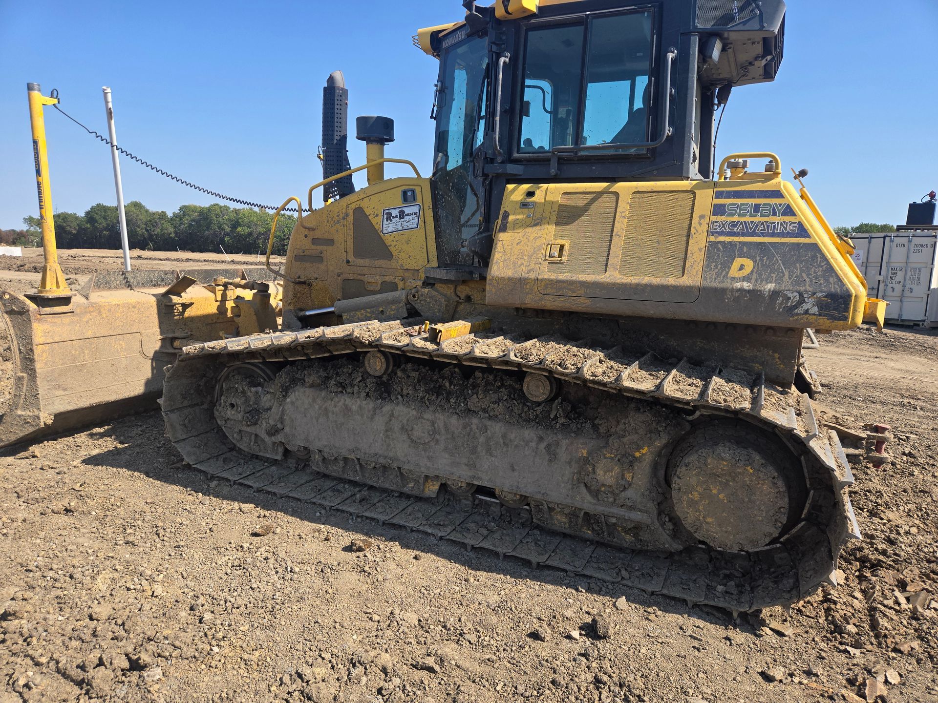 Yellow bulldozer parked on a dirt construction site under a clear blue sky.
