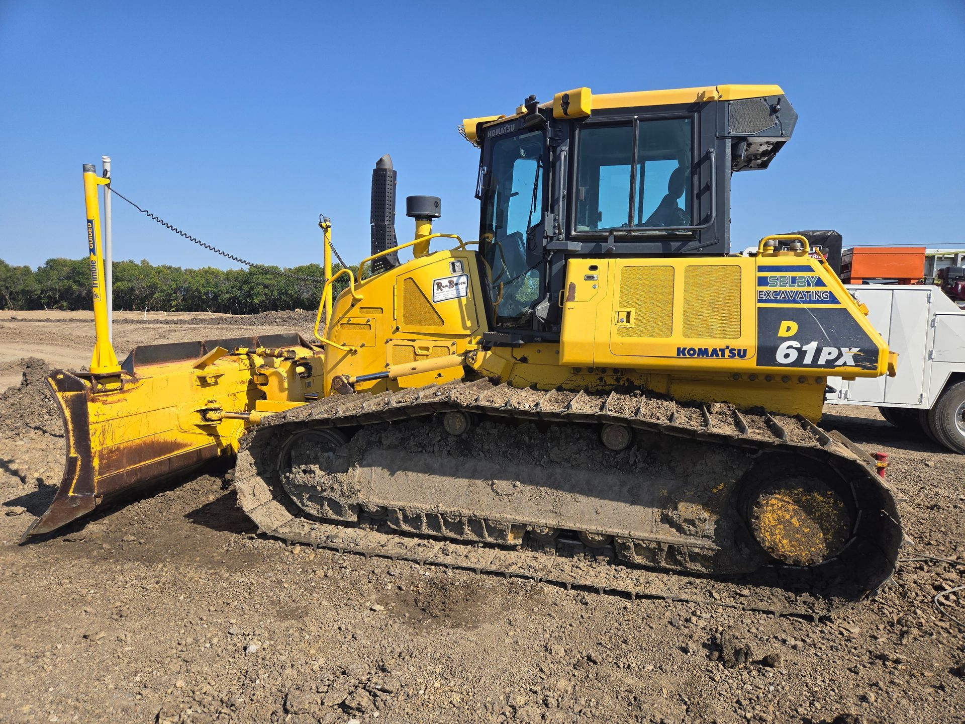 A yellow Komatsu D61PX bulldozer parked on a dirt lot against a clear blue sky.
