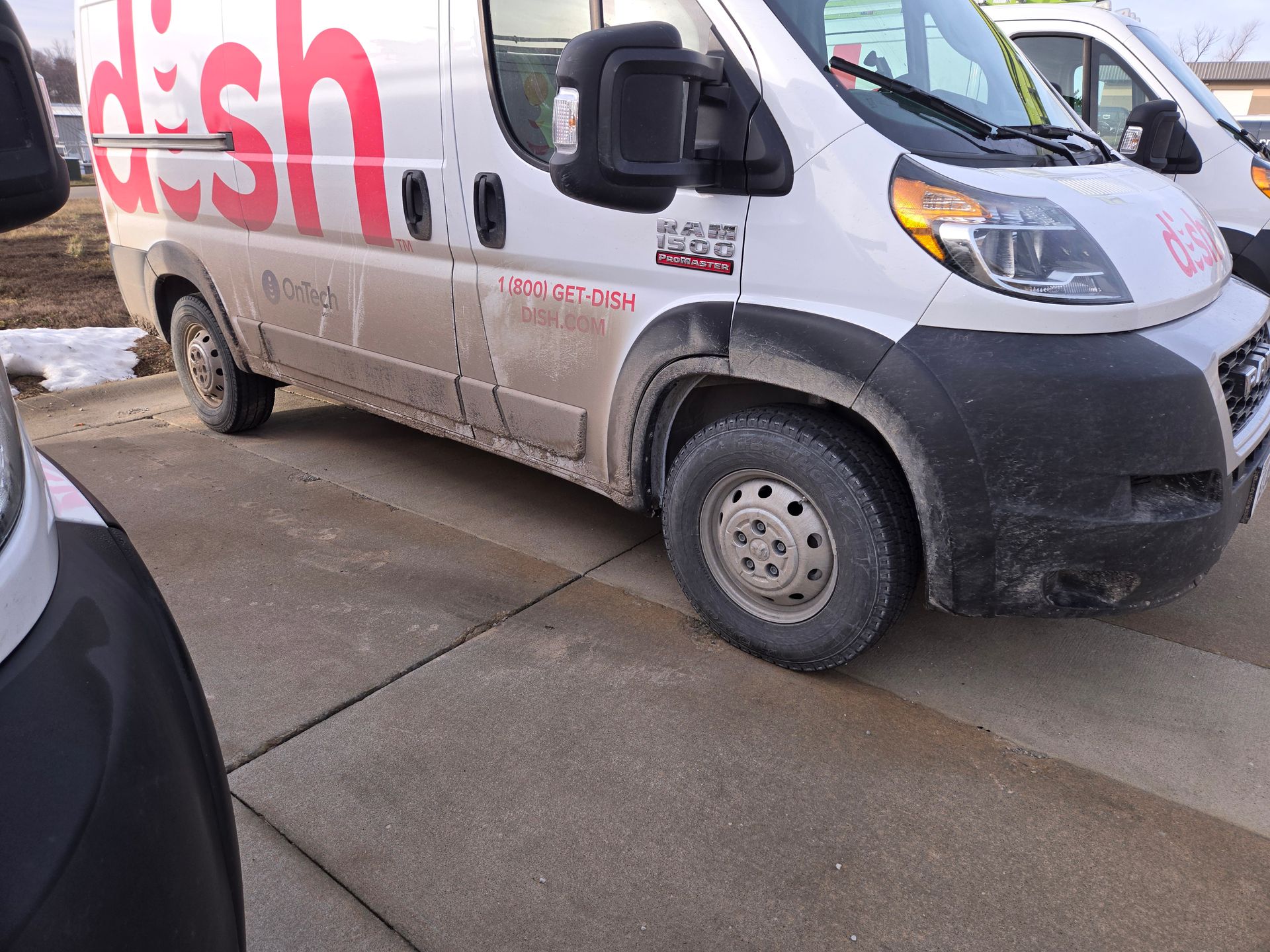A white Dish-branded van parked on a concrete surface, with a portion of another vehicle visible in the foreground.