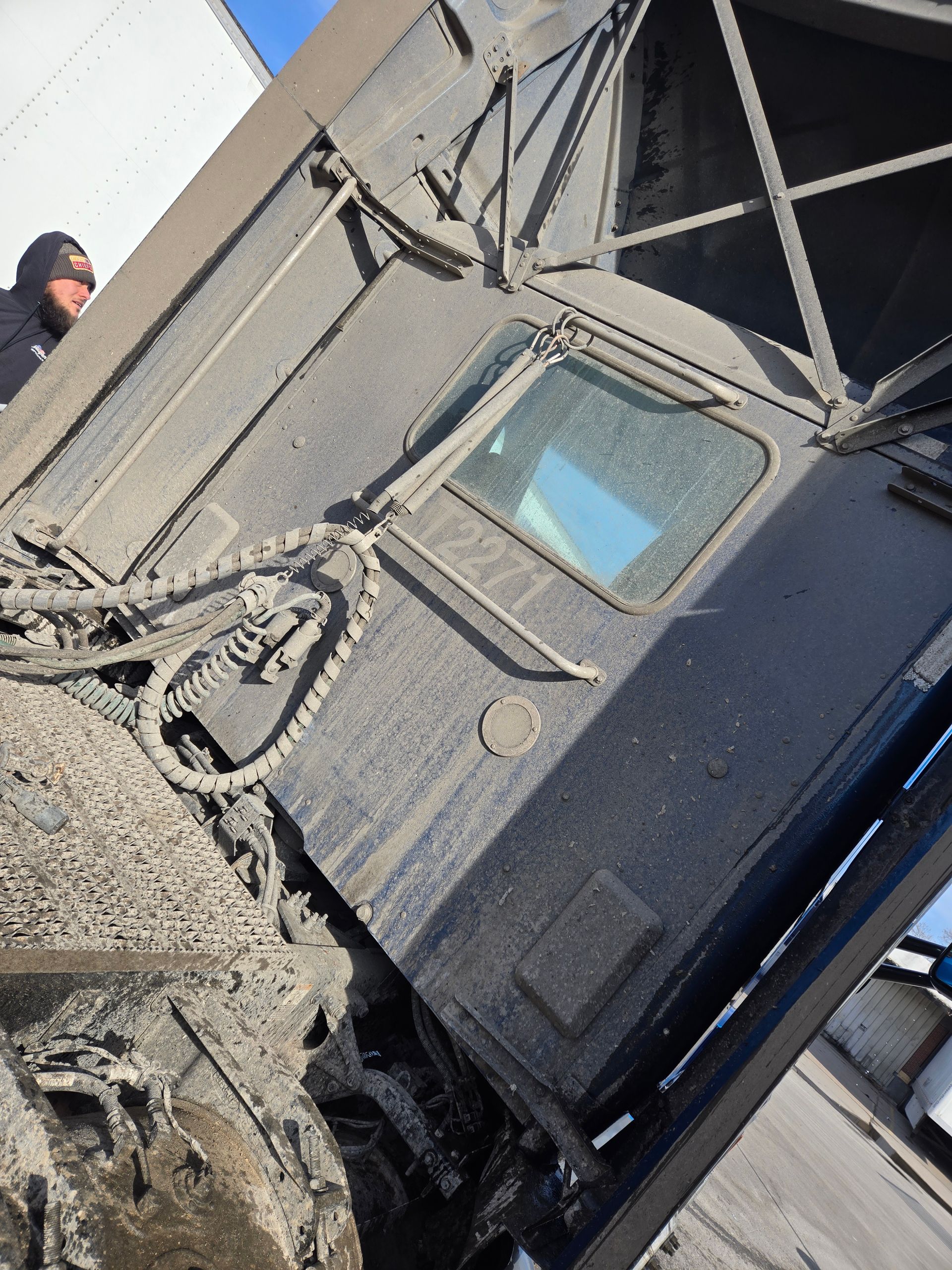 A side view of a muddy, dark-colored heavy-duty truck cab with external air hoses and a person visible in the background.