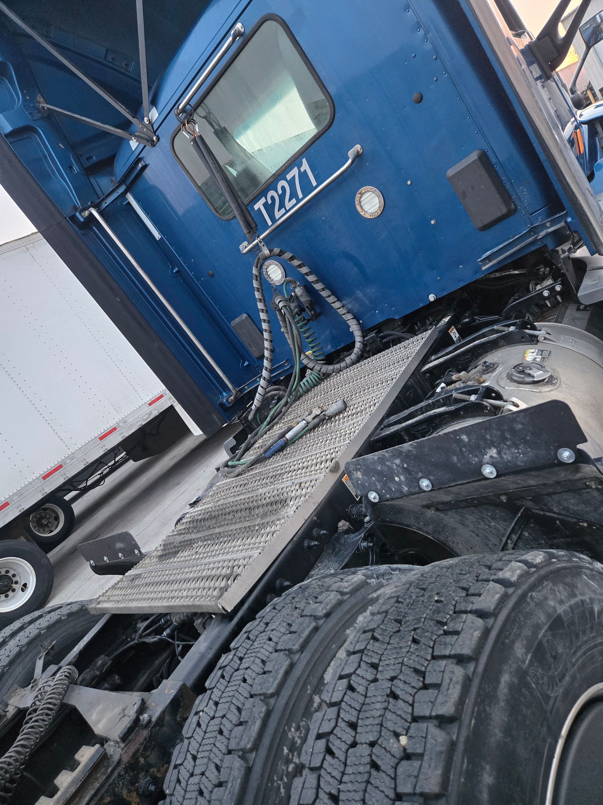 A blue semi-truck cab, viewed from the rear, showing the tire assembly and platform deck.