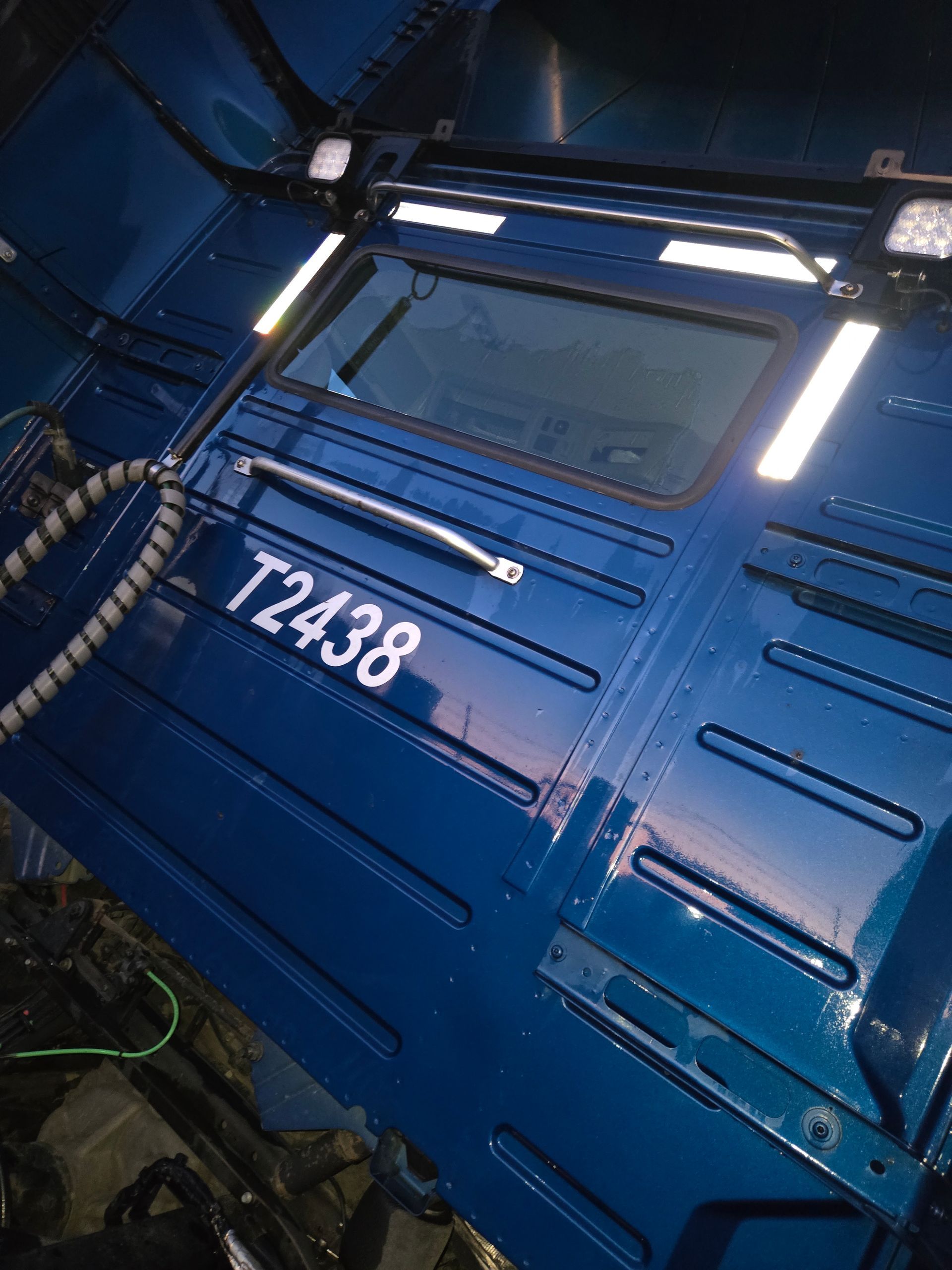 A blue semi-truck cab exterior viewed from the rear, showing a window, a grab handle, and the identification number T2438.