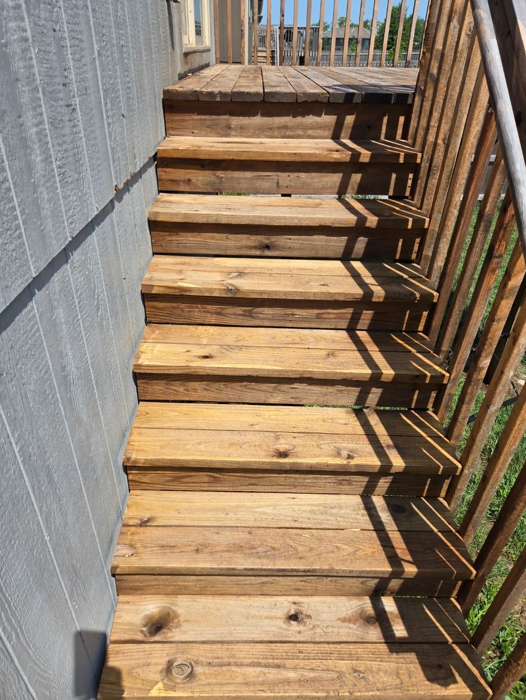 A set of weathered wooden outdoor stairs leading up to a deck, positioned beside a grey house wall.