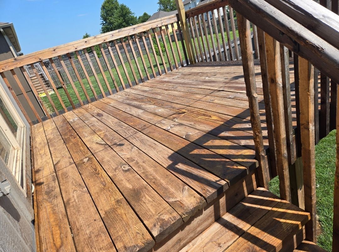 A wooden deck with a railing and stairs, viewed from an elevated angle on a sunny day.