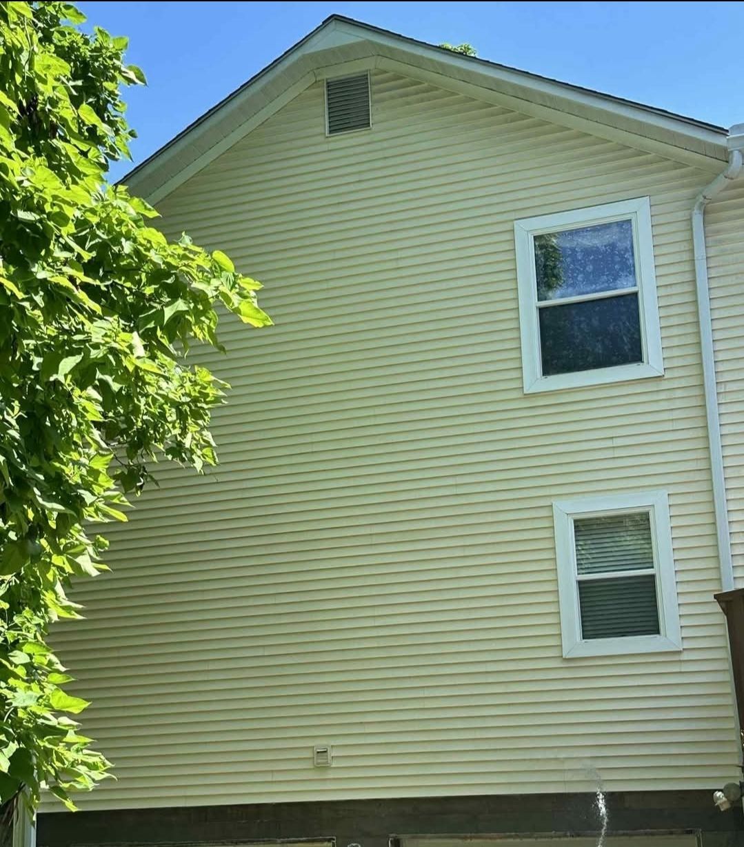 A yellow-sided two-story residential building exterior with two windows and a small attic vent under the gable roof.
