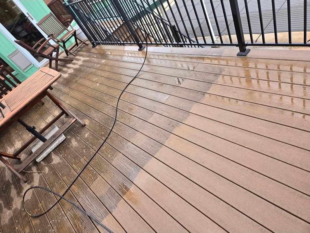 A deck showing a sharp contrast between a dirty area and a clean, power-washed section with a hose lying across the surface.