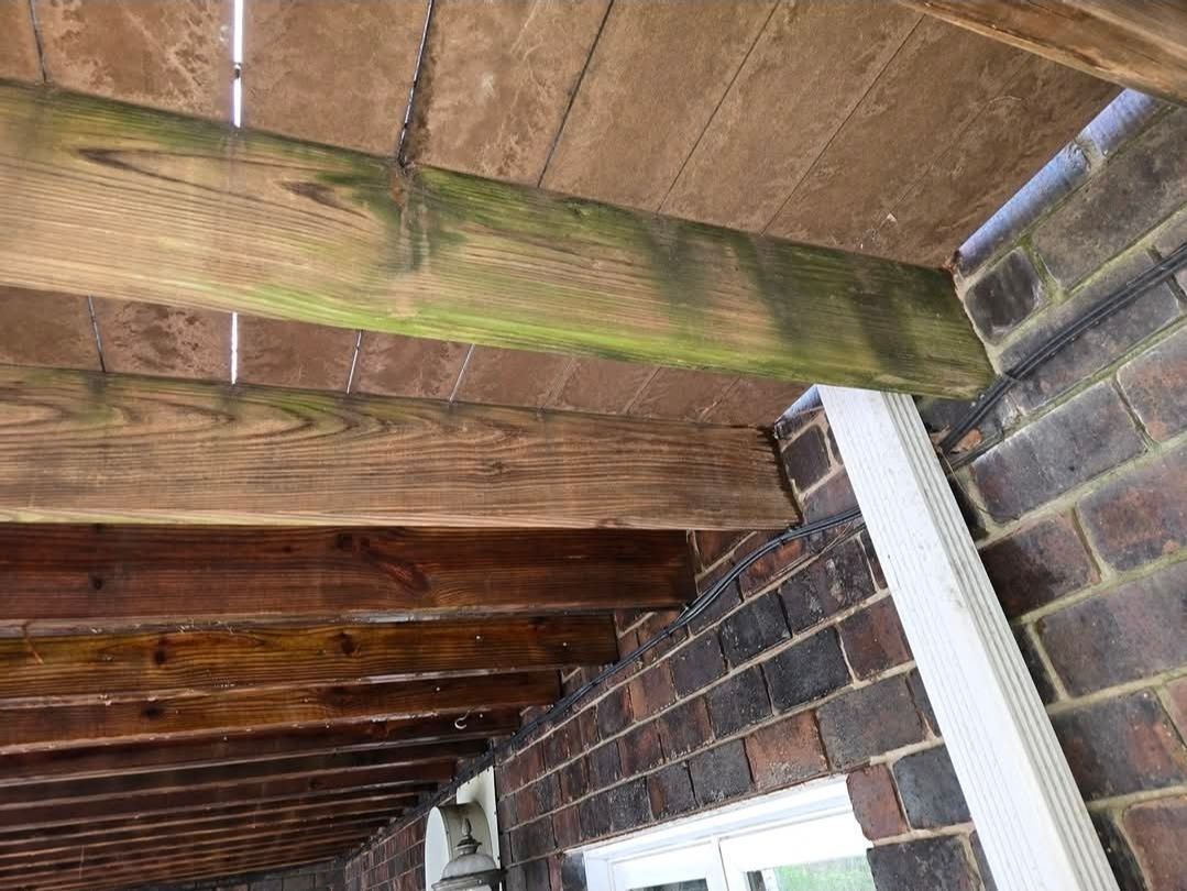 Low-angle view of wooden deck beams attached to a brick wall with a white downspout on the right.