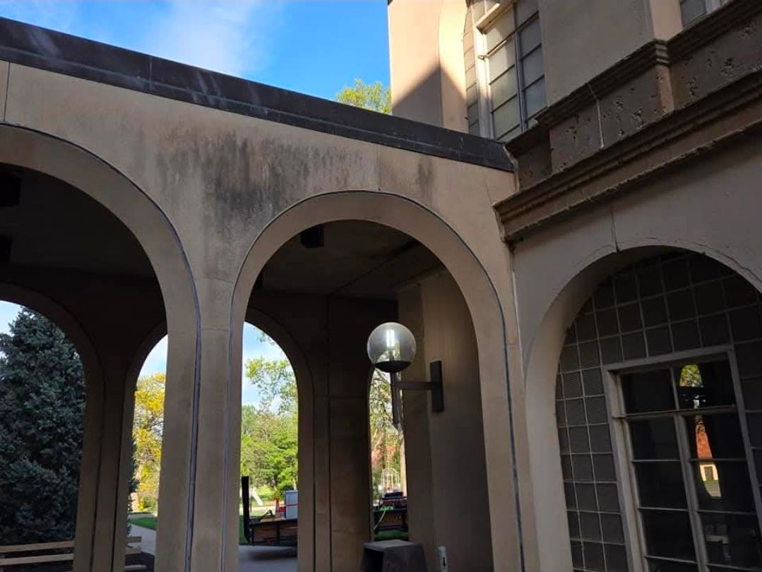 Beige arches of a building facade with a spherical light fixture, leading to an outdoor courtyard with trees.